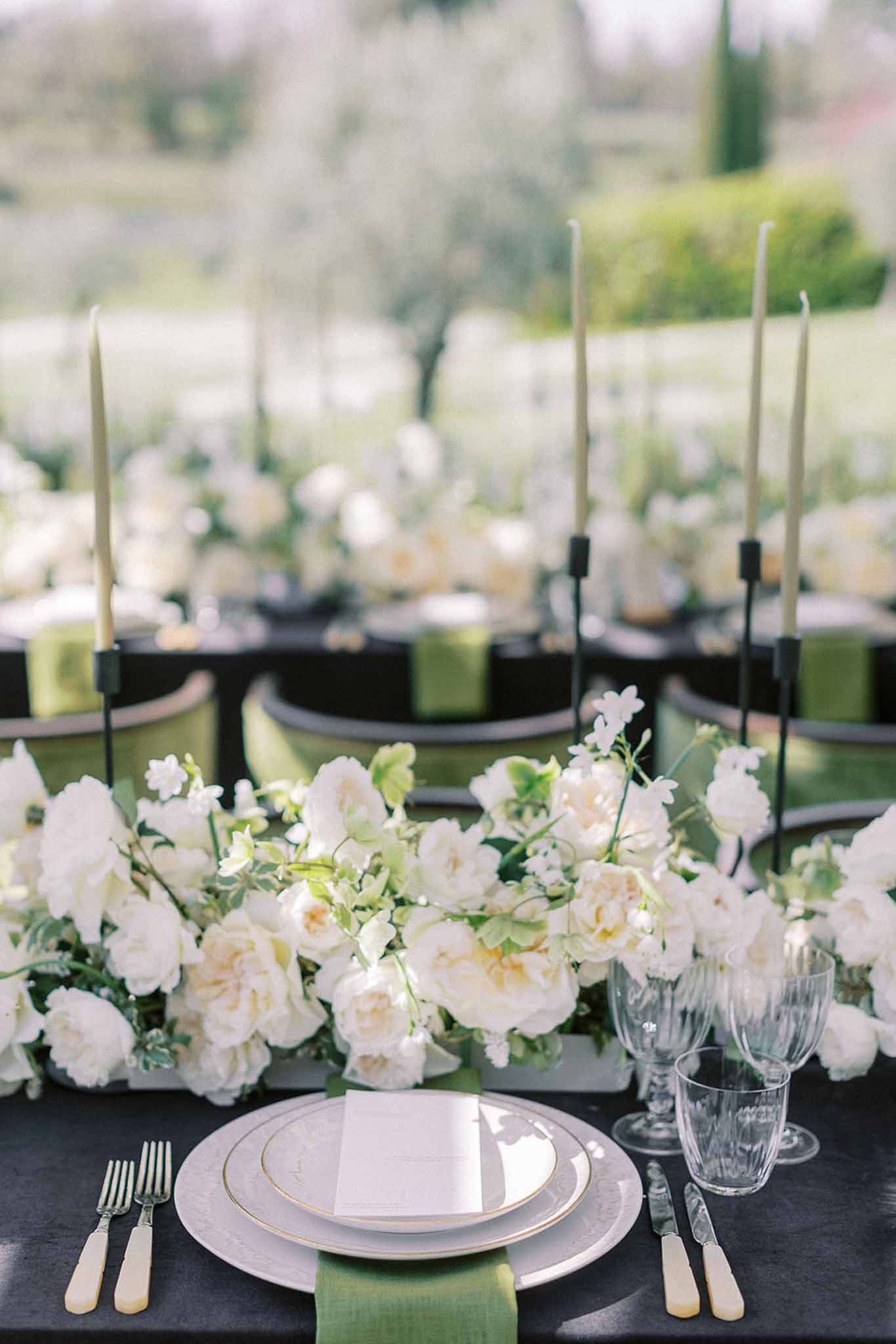 Reception place setting with gold-rimmed plates, green napkin, and cream rose runner on charcoal linen