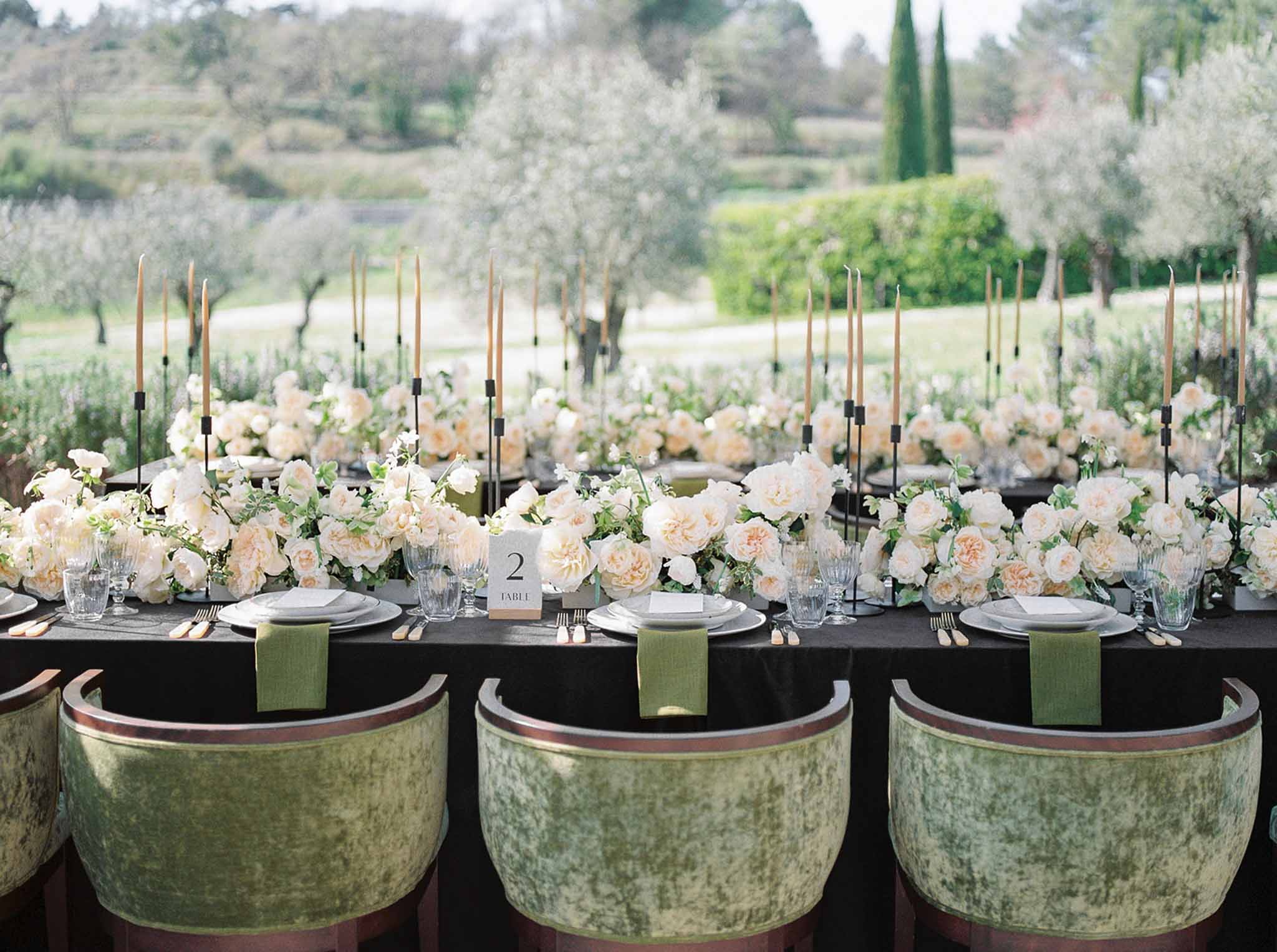 Outdoor reception table with cream and blush rose runner, sage green velvet chairs, and black linen tablecloth