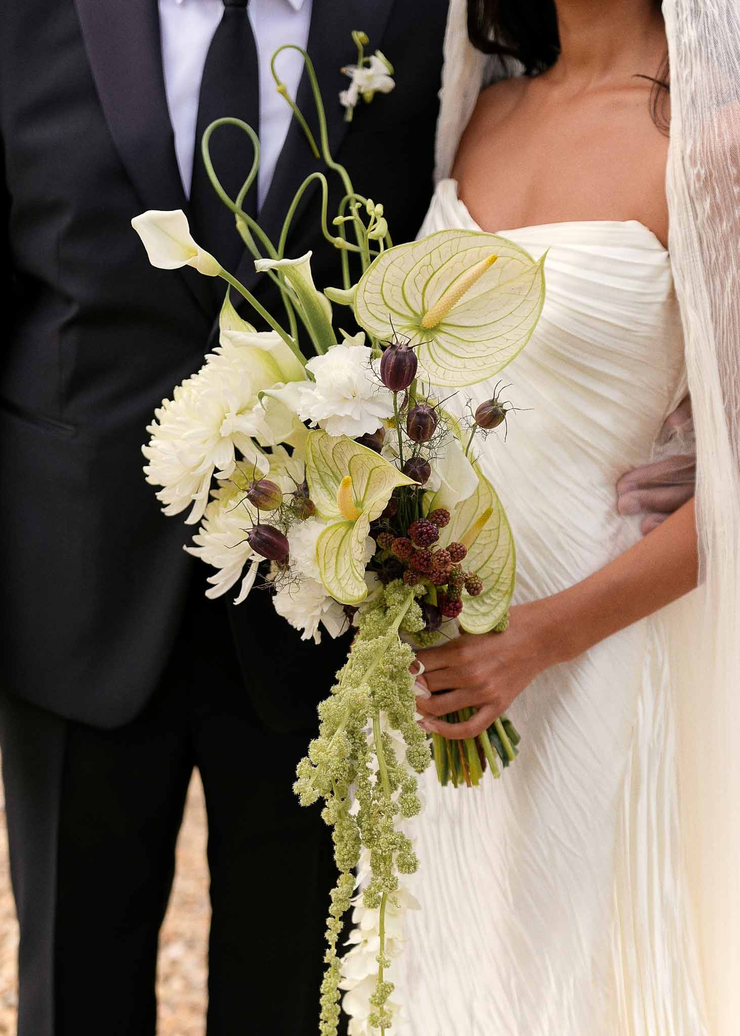 Oversized bouquet of green anthurium, white calla lilies, burgundy fritillaria, and trailing amaranthus at bride's side