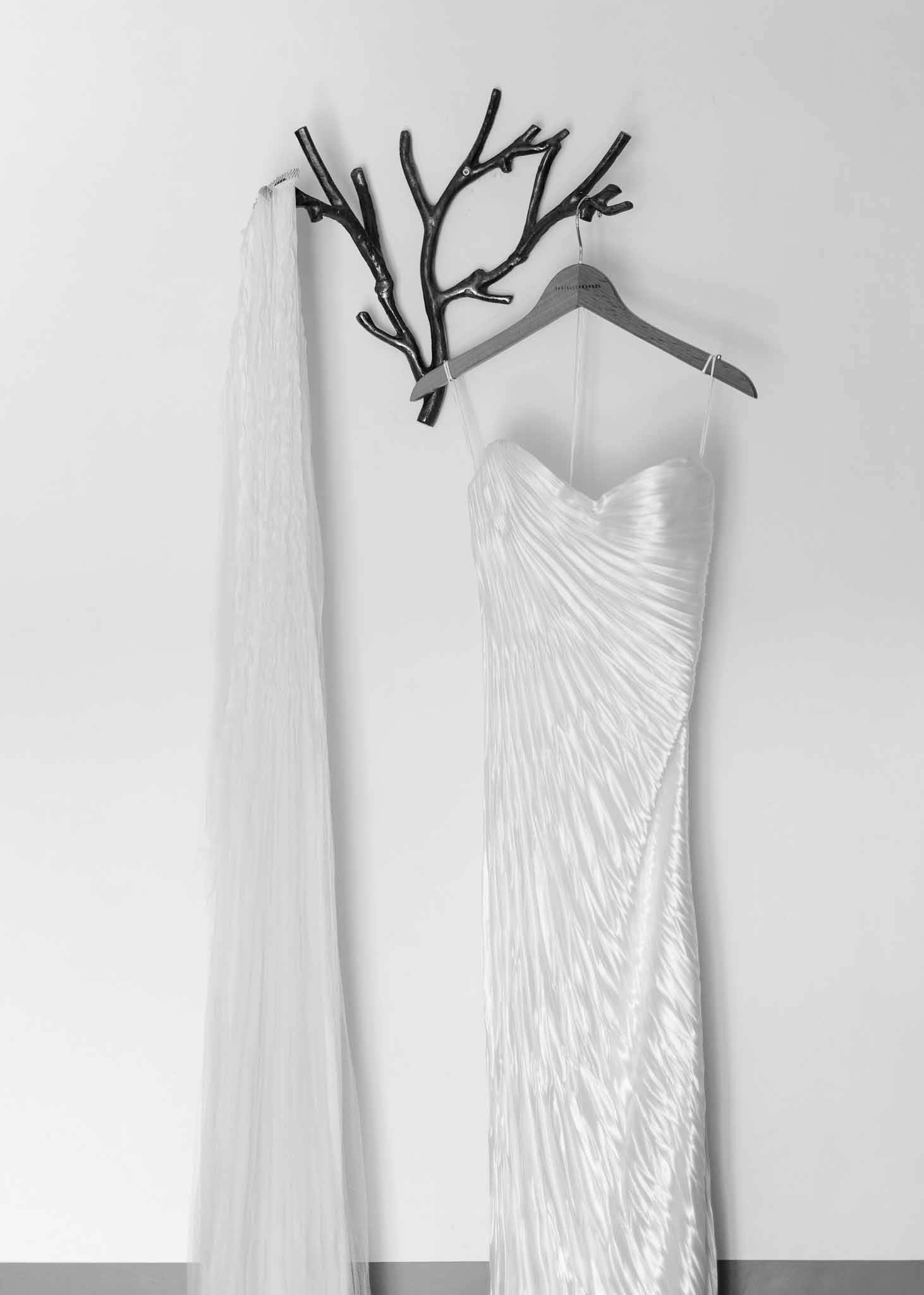 Black and white wedding dress with draped bodice and cathedral veil hanging from branch wall hook
