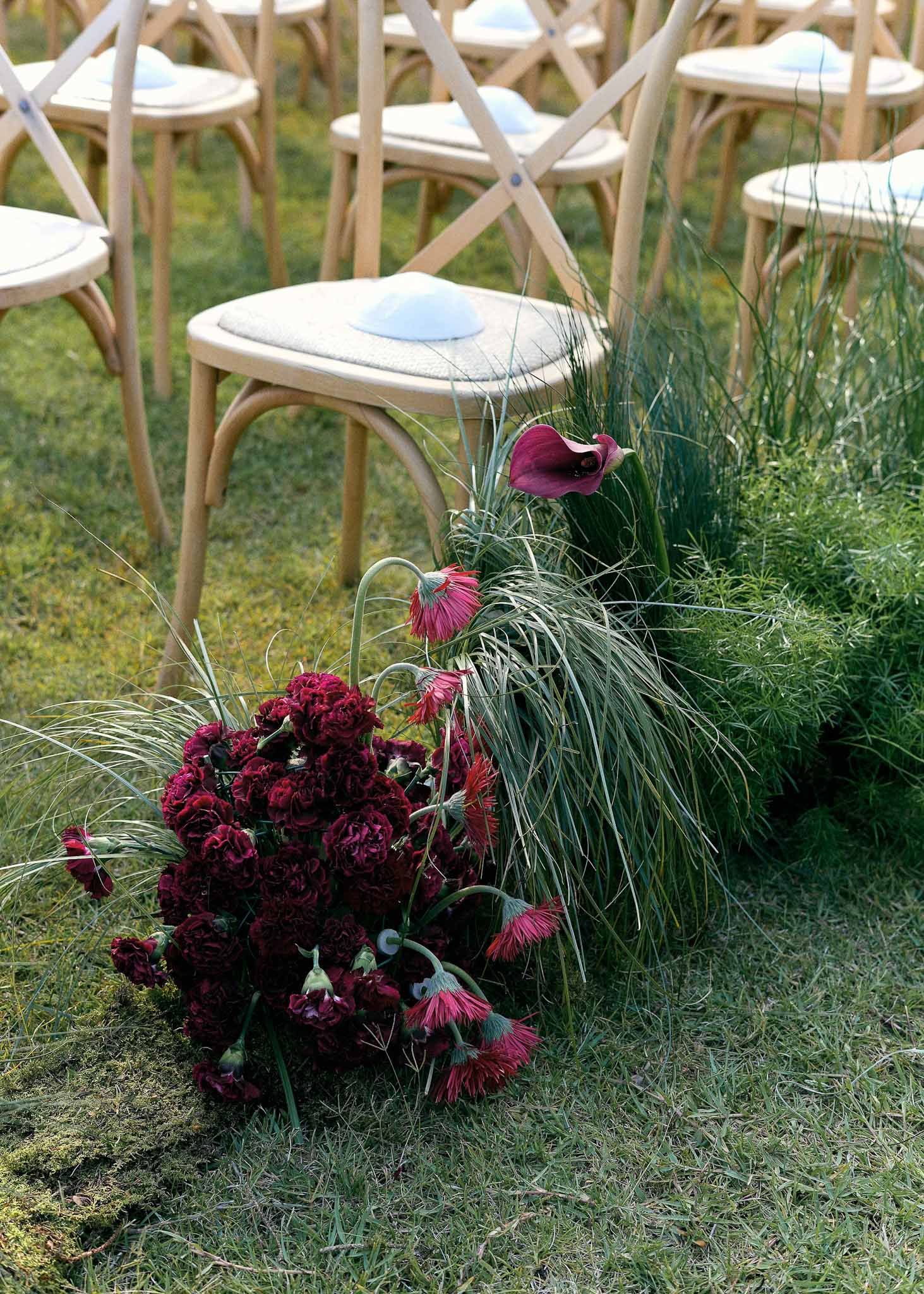 Ceremony aisle floral arrangement with burgundy carnations and pink gerbera daisies on grass lawn