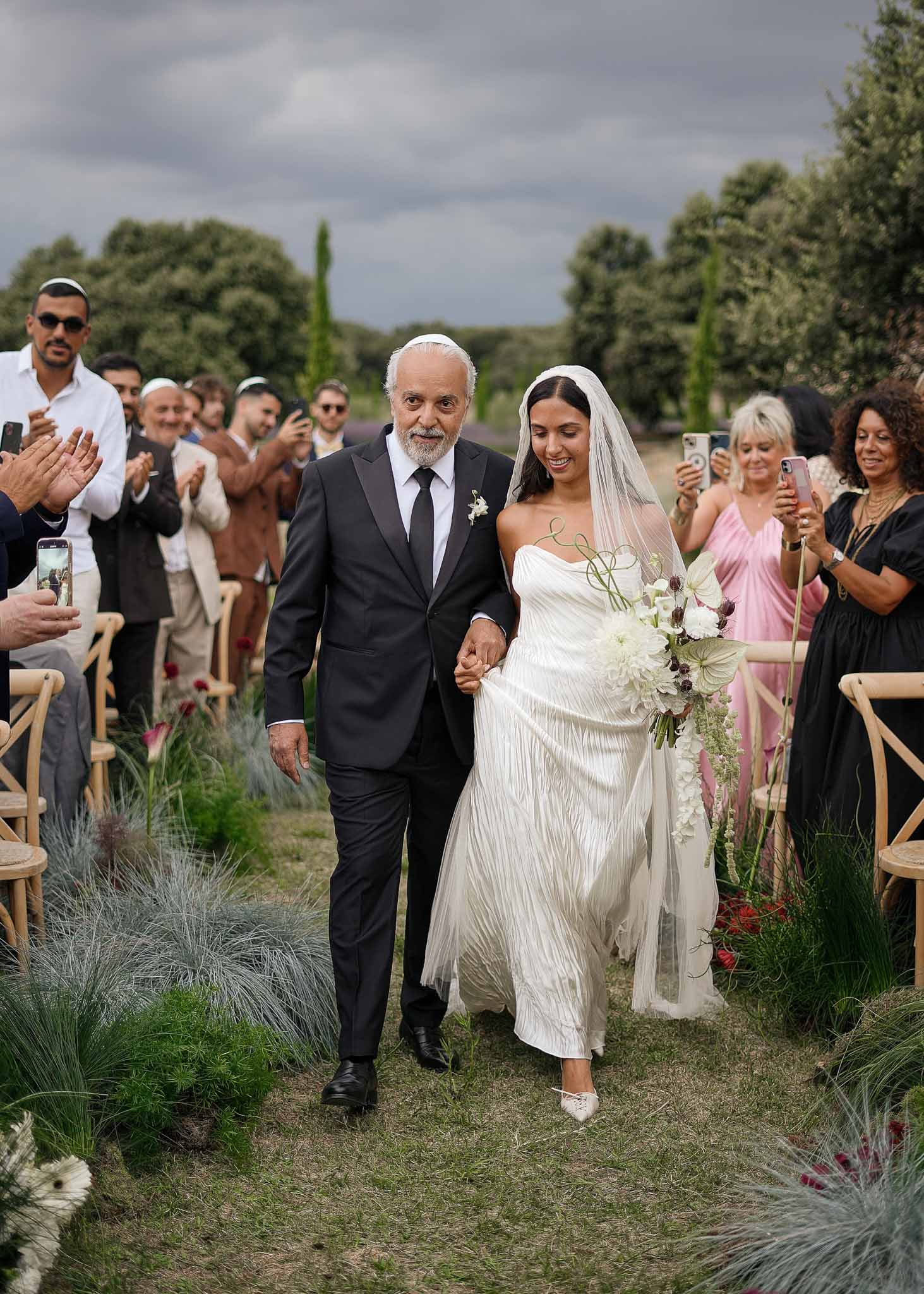 Father in kippah walking bride down aisle with white dahlia and burgundy accent bouquet