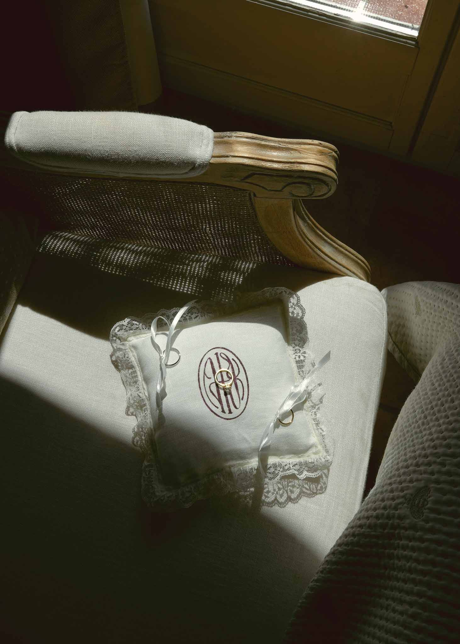 Two gold bands on monogrammed linen ring pillow with lace trim and satin ribbon on gilt armchair