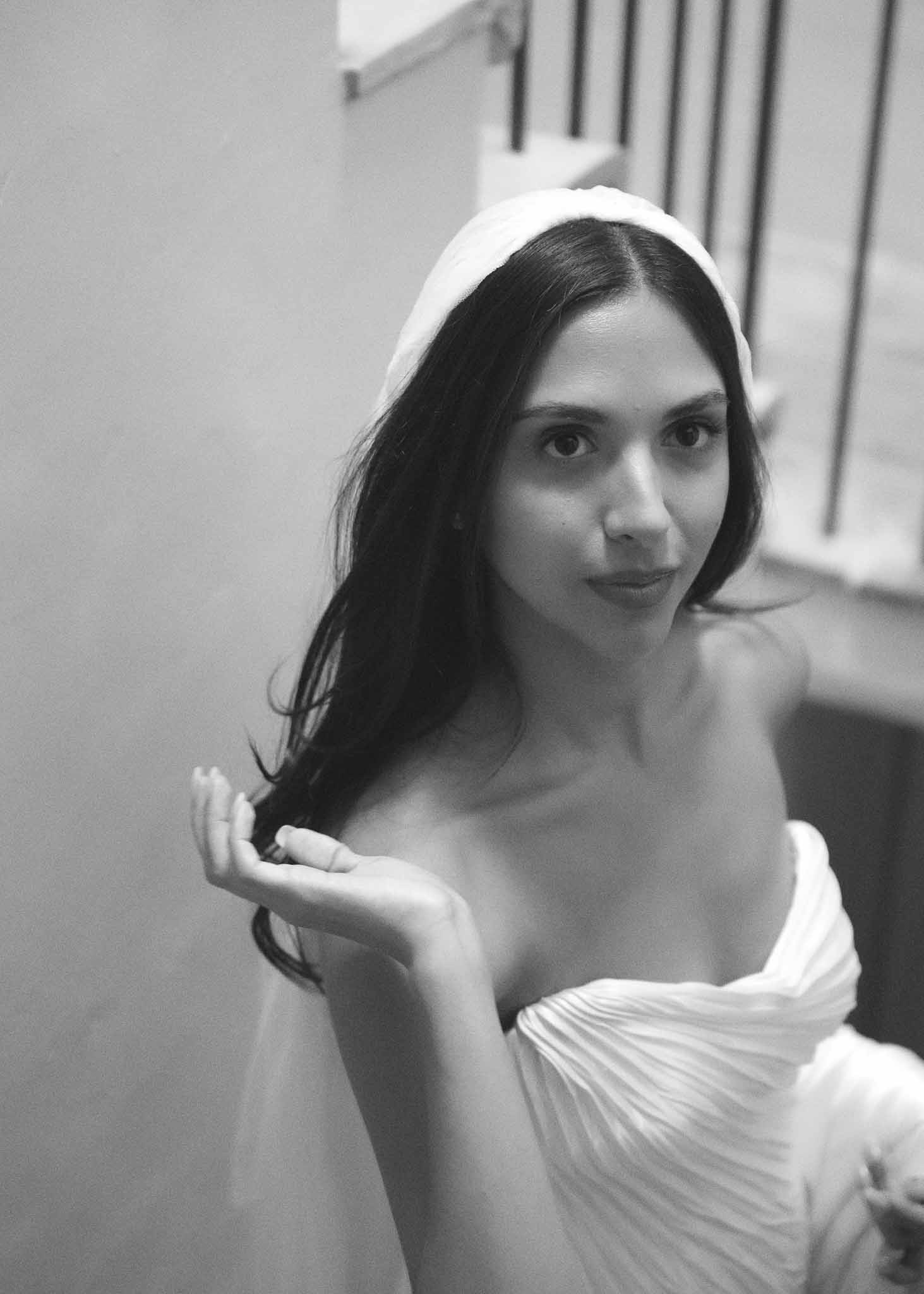 Black and white portrait of bride in strapless pleated gown with padded headband on interior staircase