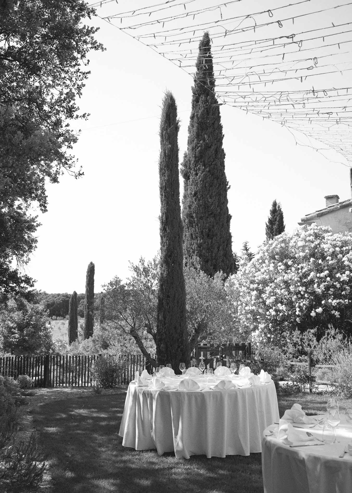 Black-and-white outdoor reception setup with round tables, white linens, and fairy lights strung above a garden