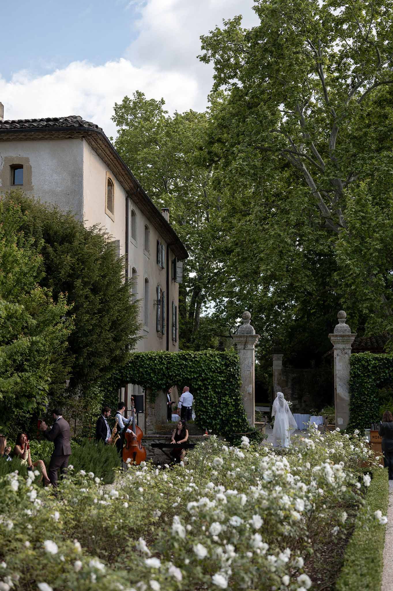Jazz trio performs in formal rose garden as bride in veil enters through stone gate at French estate
