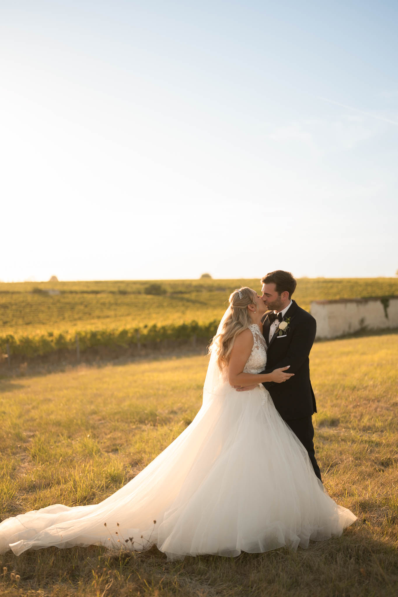 Bride and groom kissing in golden hour light with vineyard rows in the background