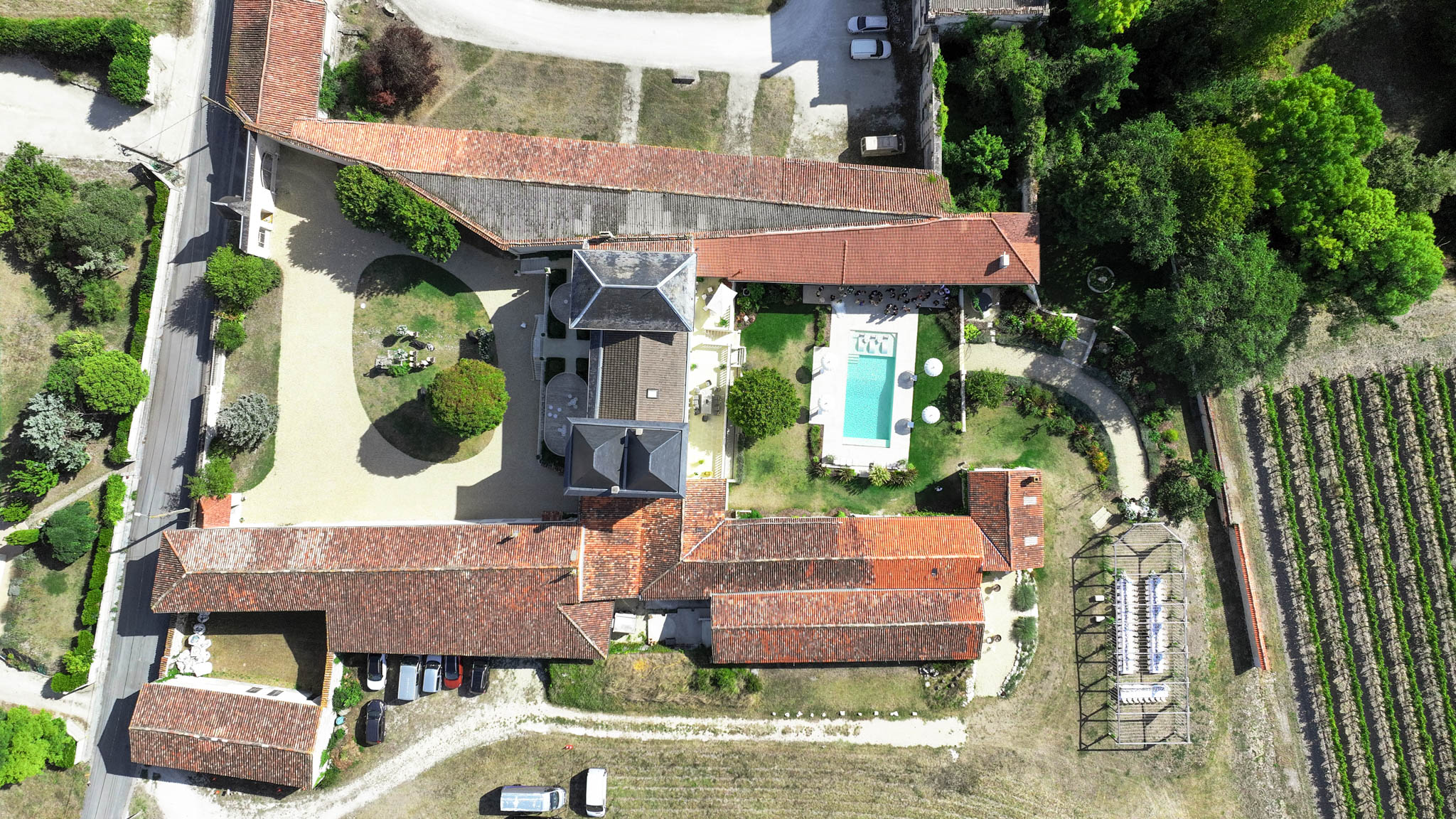Aerial view of country estate with slate-roofed manor, pool, barn, and vineyard rows from directly above