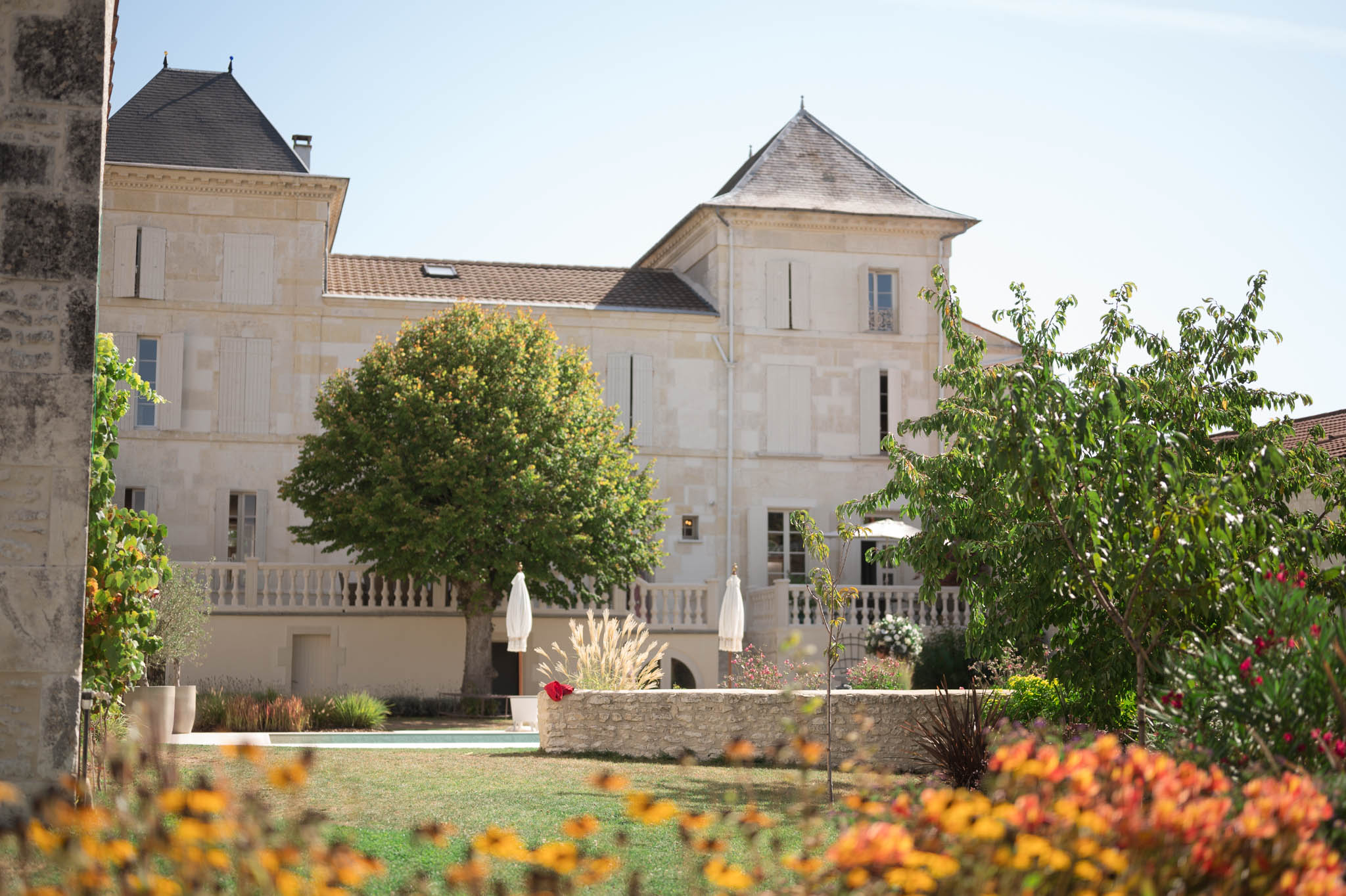 Cream limestone chateau with slate turret roof pool white parasols and ornamental grasses framed by yellow flowers