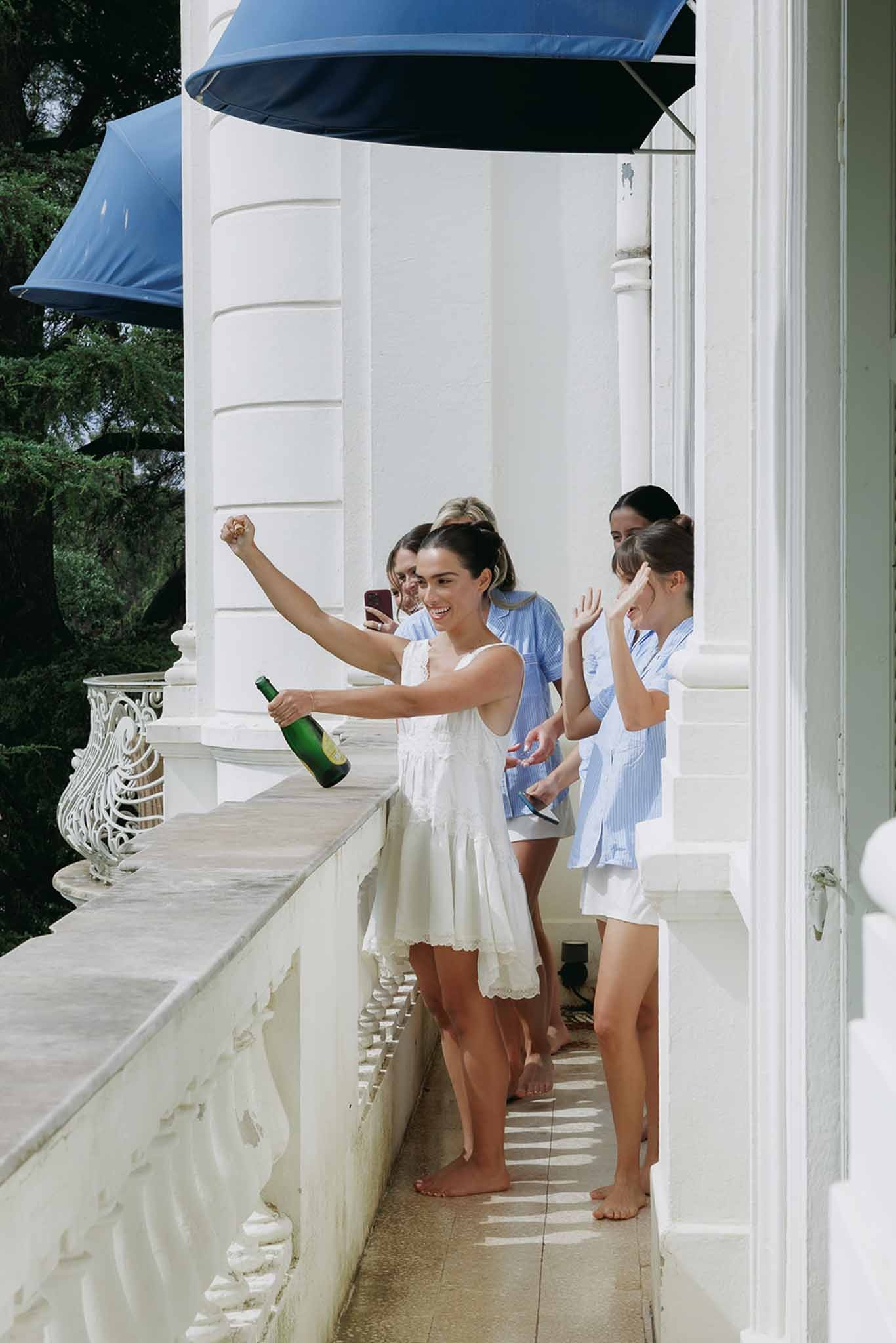 Bride popping champagne on balcony with bridesmaids at Domaine Rocabella, Cote d'Azur