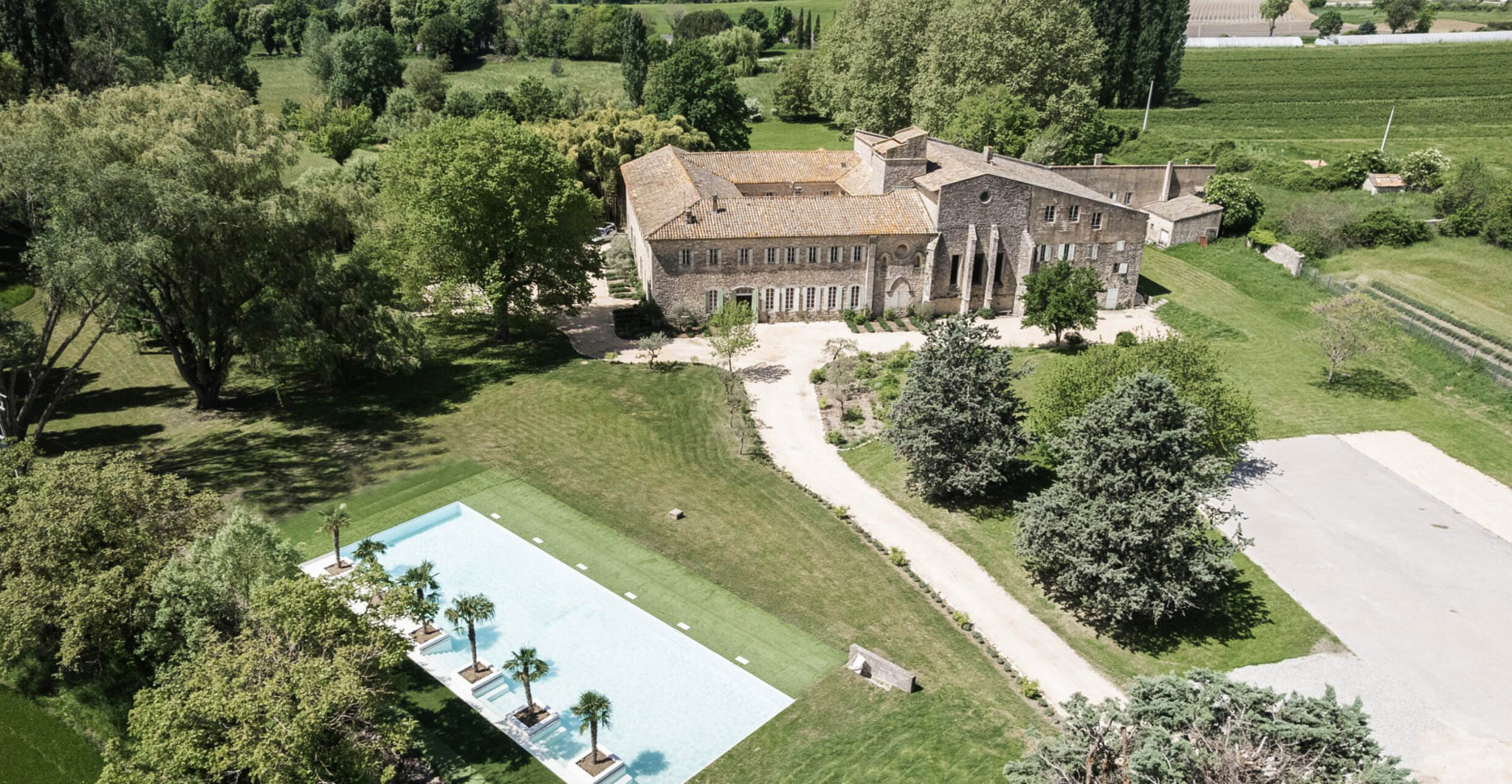 Aerial drone view of a stone Provencal property with terracotta roofs, infinity pool, and surrounding vineyards