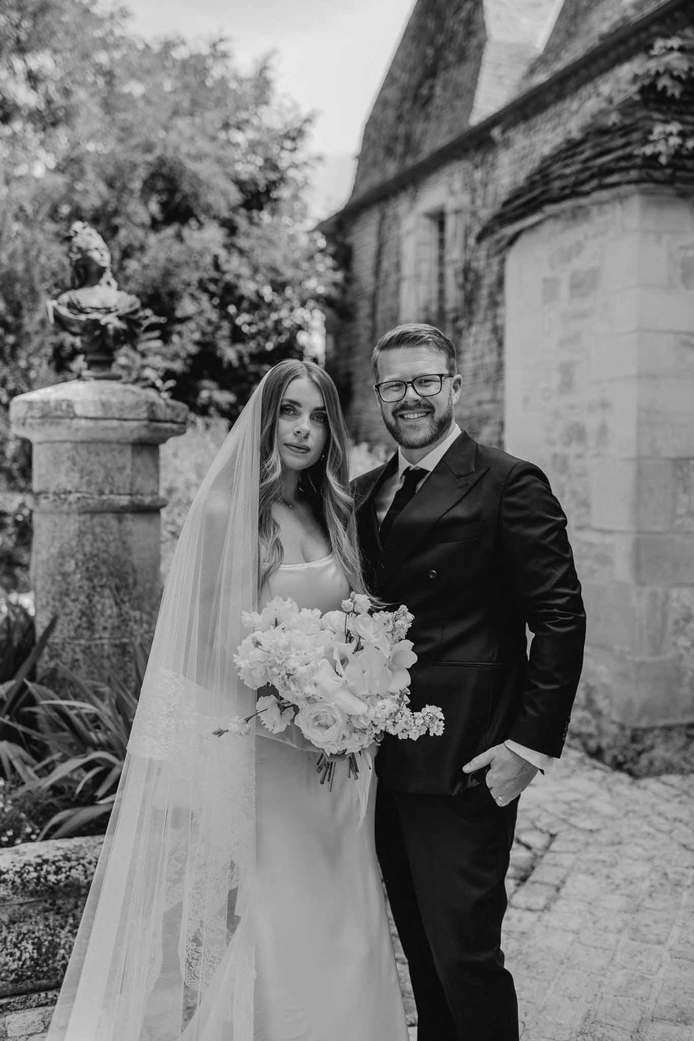 Black and white couple on cobblestone path with bride holding peony bouquet and lace-trimmed veil