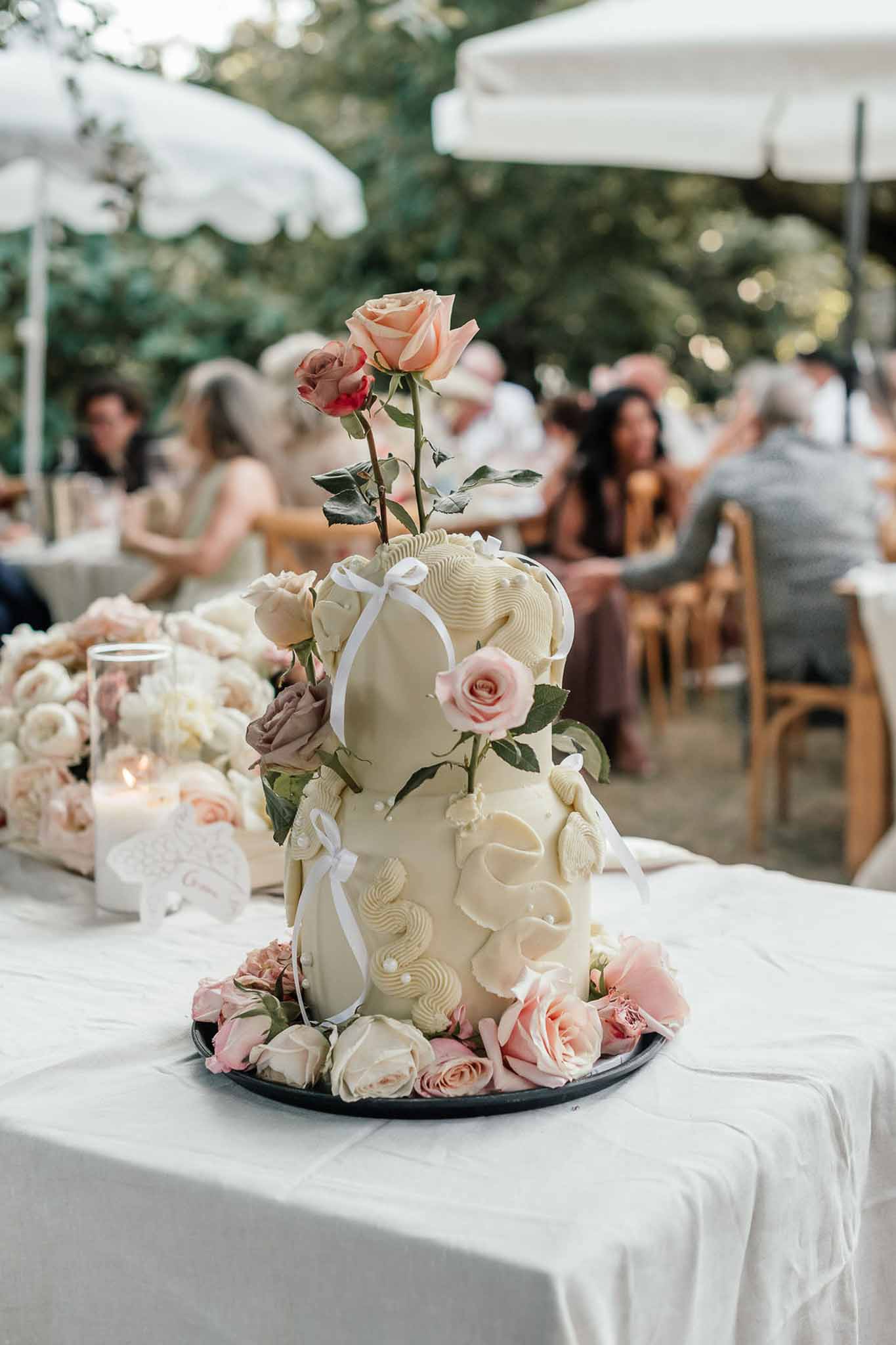 Single-tier ivory cake with wave piping and pearl details surrounded by blush and dusty rose blooms
