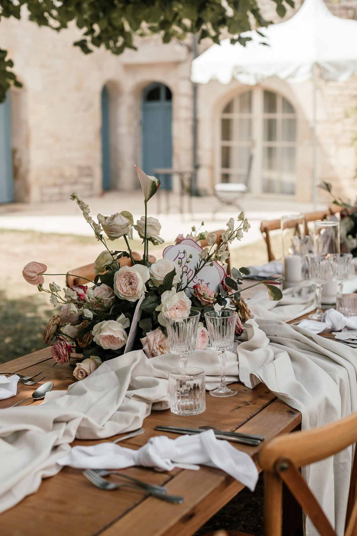 Farm table with blush garden rose sweet pea and anthurium centerpiece crystal glasses and cross-back chairs