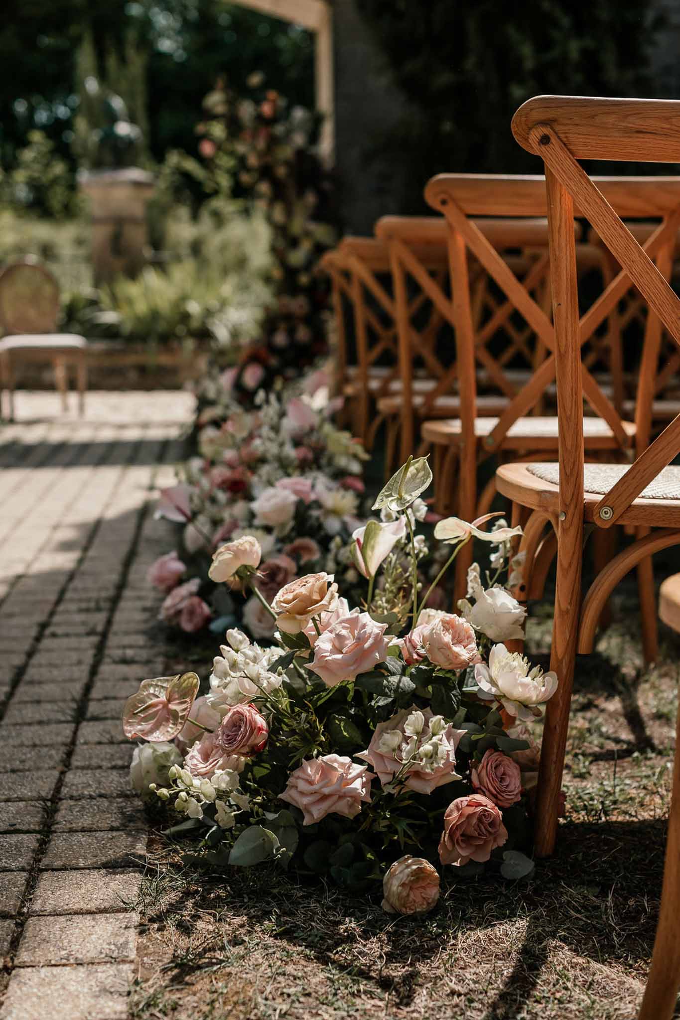 Ground-level ceremony aisle florals with blush roses, ranunculus, and anthurium on cobblestones