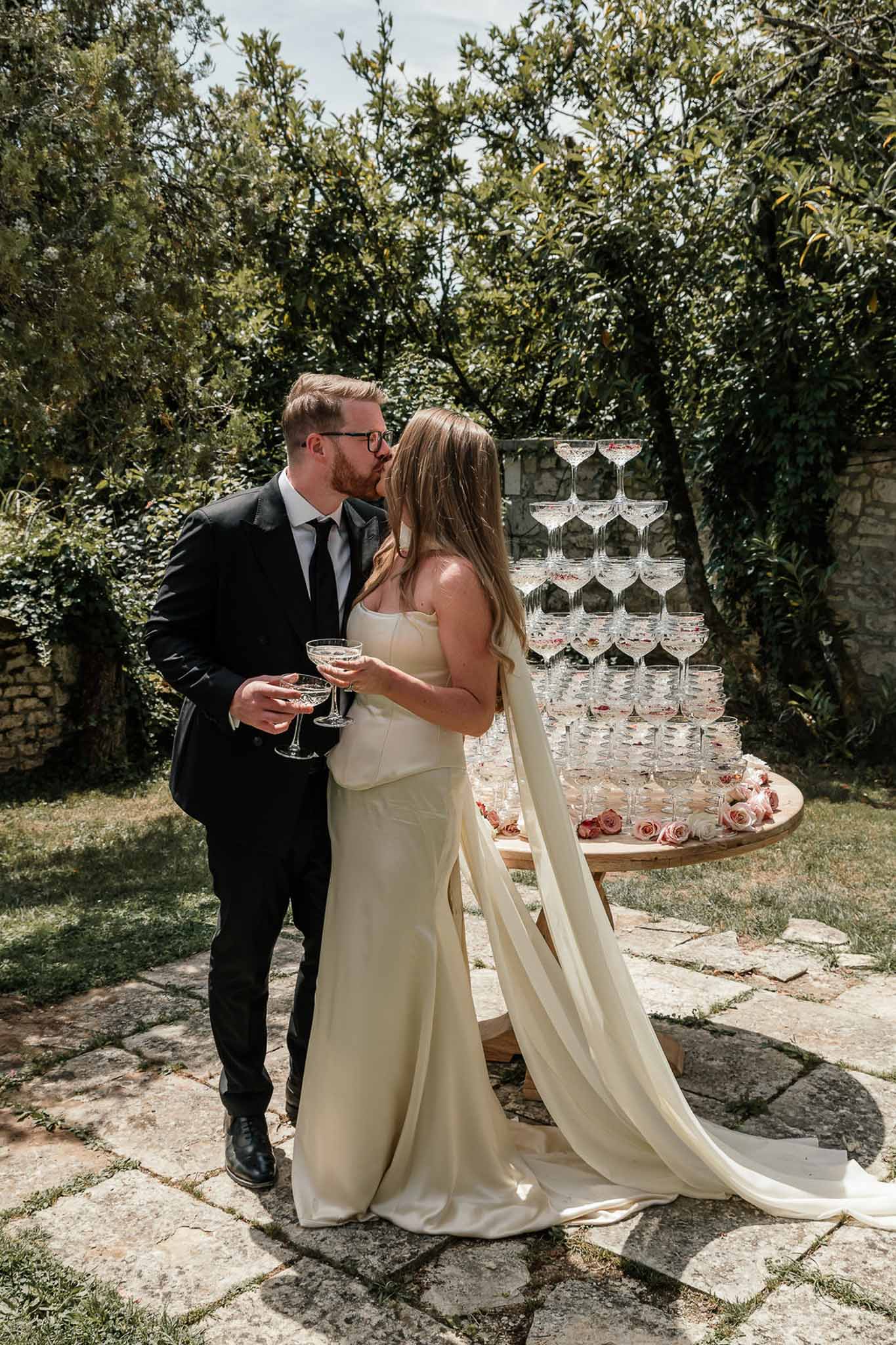 Bride and groom kissing beside champagne tower decorated with blush and dusty pink roses