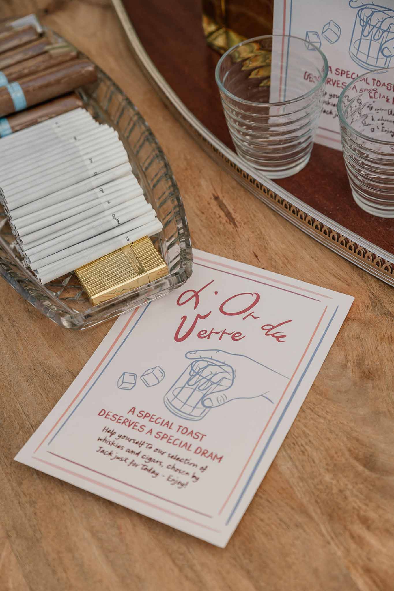 Whisky and cigar station with custom printed card, crystal tumblers, and gold lighter on wooden table