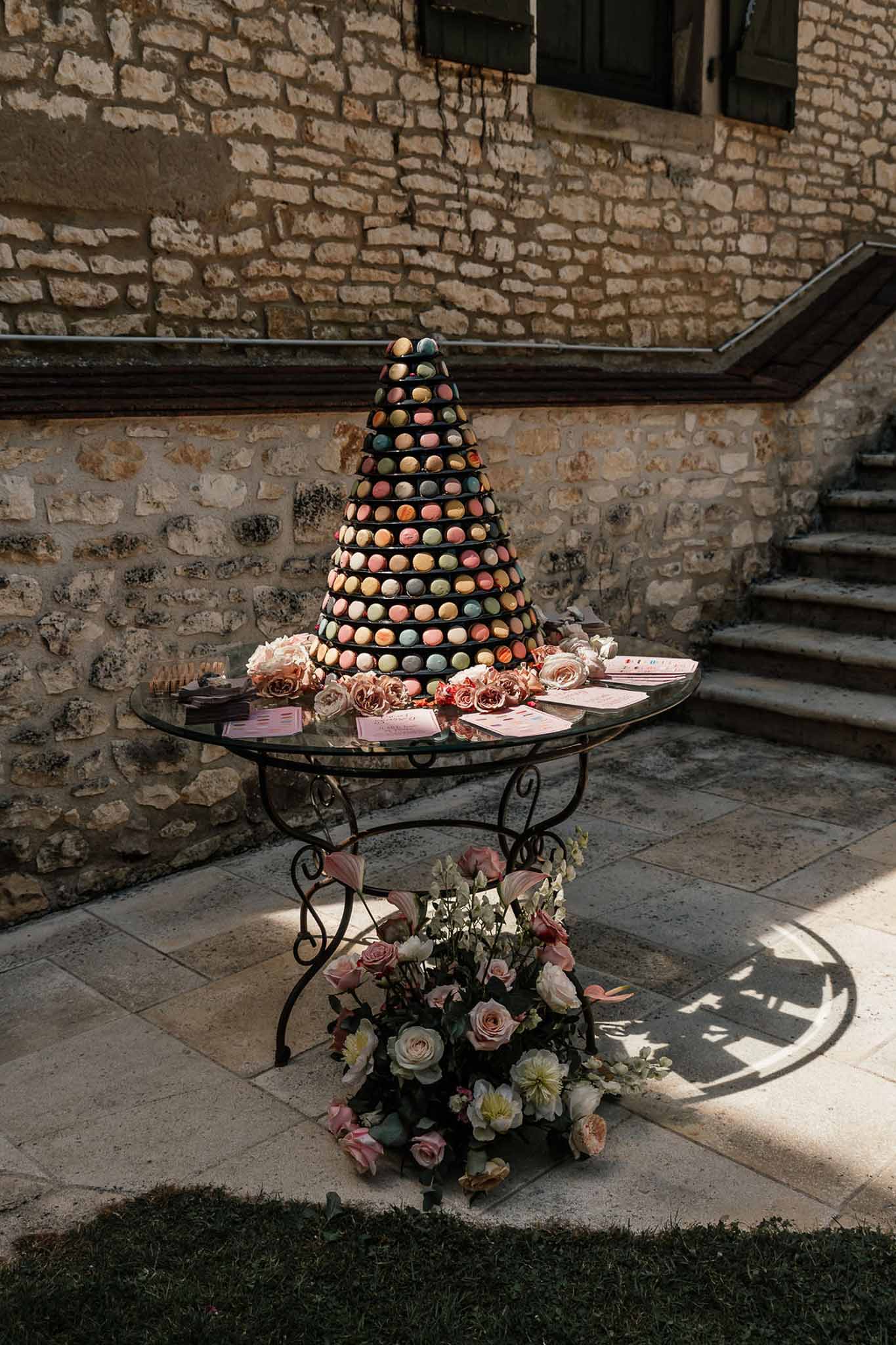 Multicoloured macaron tower on iron table with scattered blush roses, sage and yellow macarons, and pink menu cards