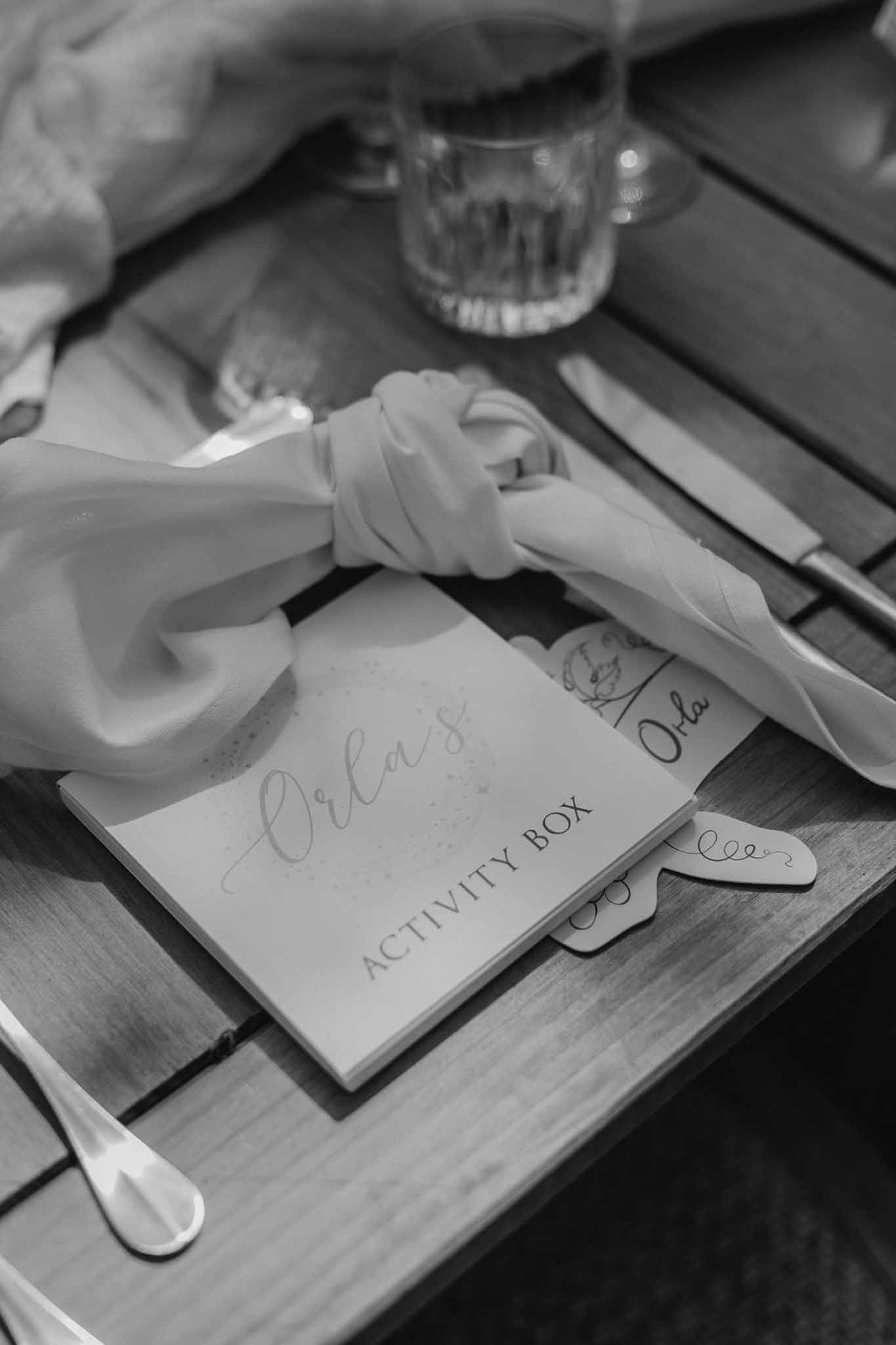 Black and white close-up of child's personalised activity box with silk ribbon at wedding table