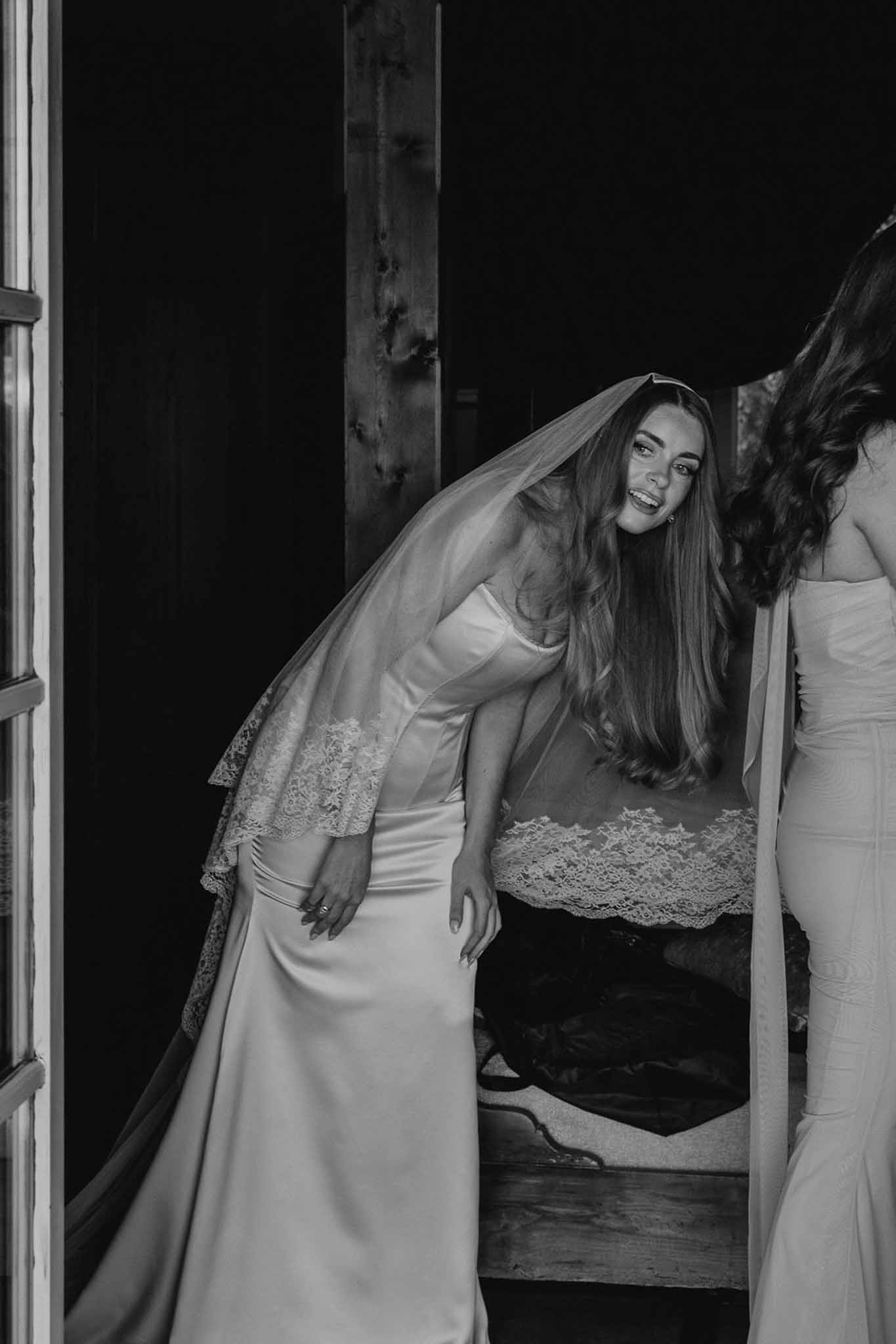 Black and white candid portrait of bride laughing in doorway wearing satin gown with lace veil