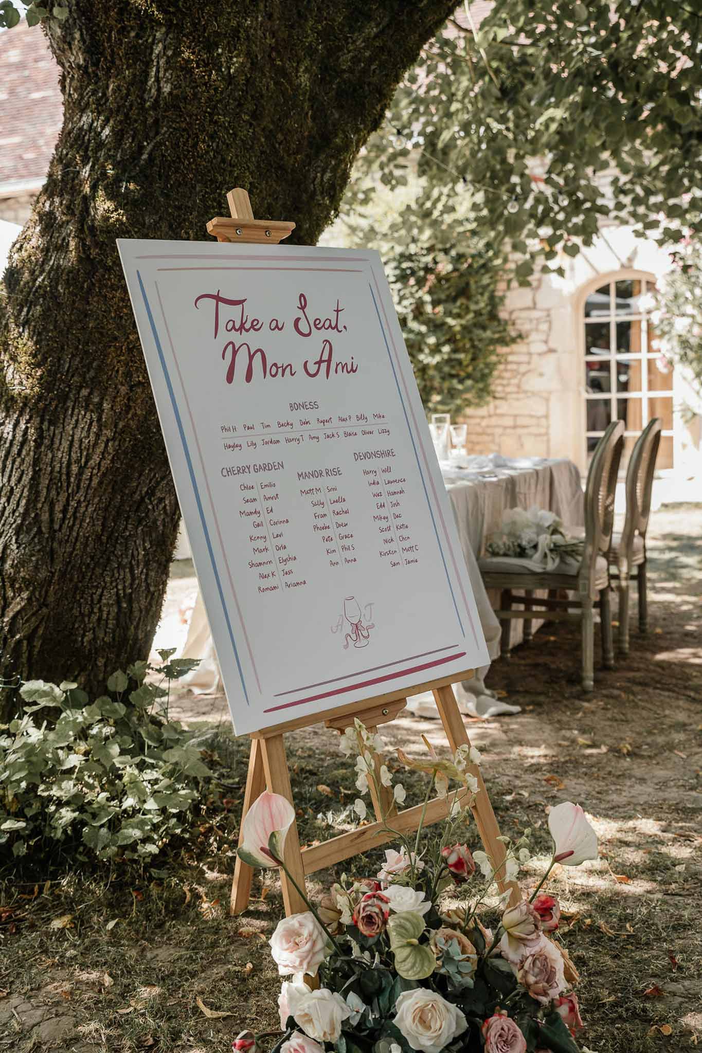 Seating chart sign reading Take a Seat Mon Ami with blush rose arrangement at base on easel