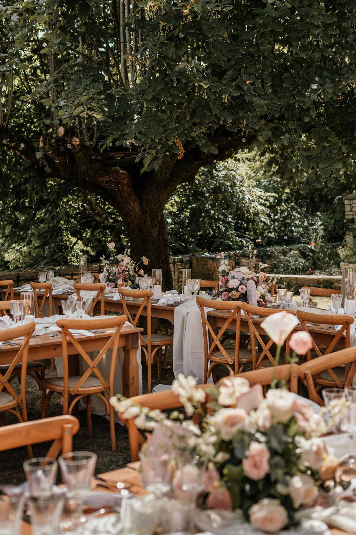 Outdoor reception tables with wooden cross-back chairs, blush rose centerpieces, and grey linen runners