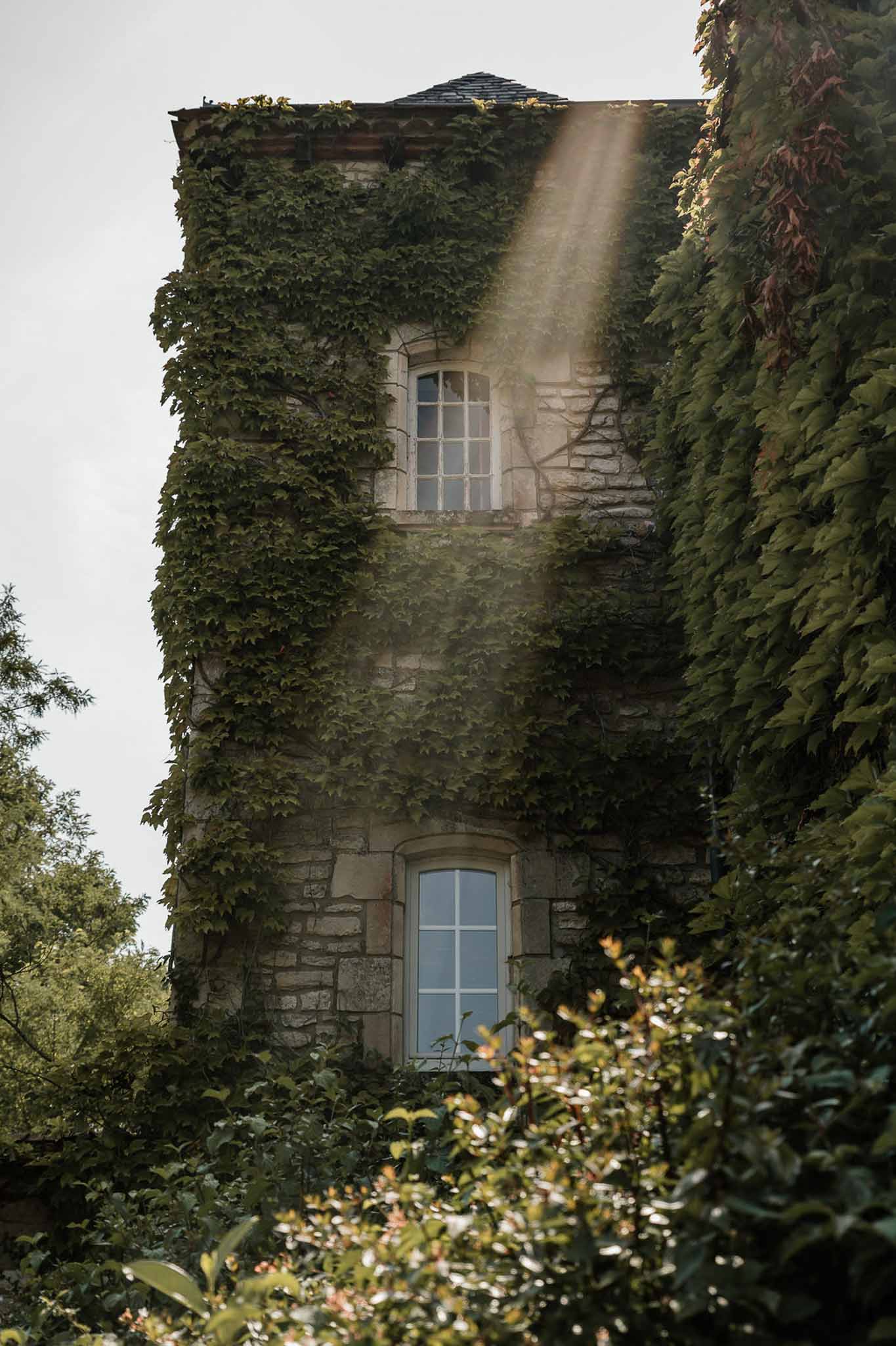 Ivy-covered chateau stone tower with arched windows and slate turret in diagonal sunlight