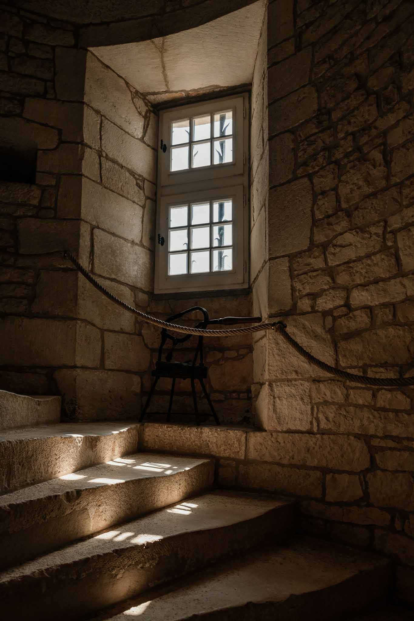Curved stone spiral staircase inside a chateau tower with rope handrail and natural light from a casement window