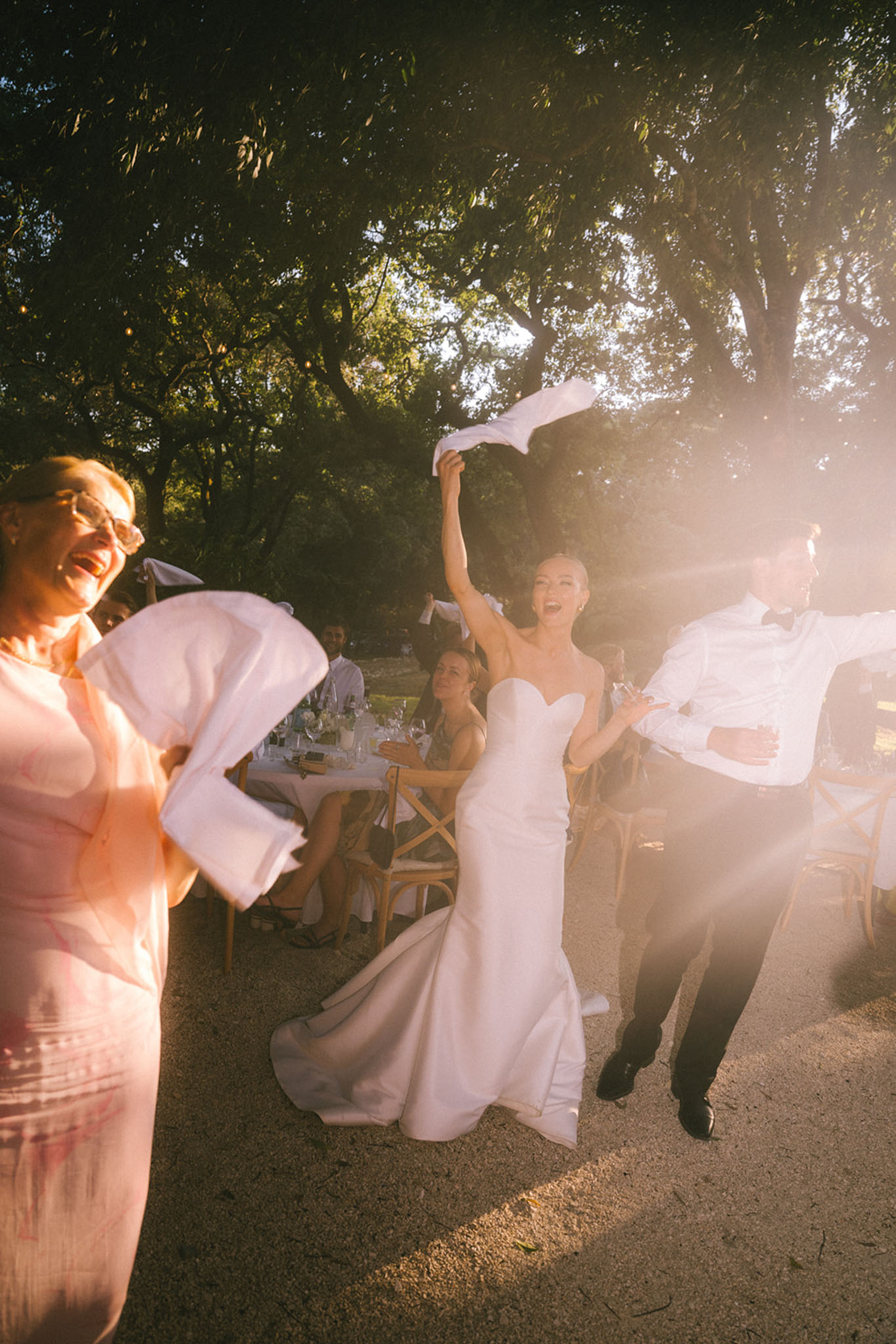 Bride and groom waving white napkins during outdoor reception dinner with guests at golden hour