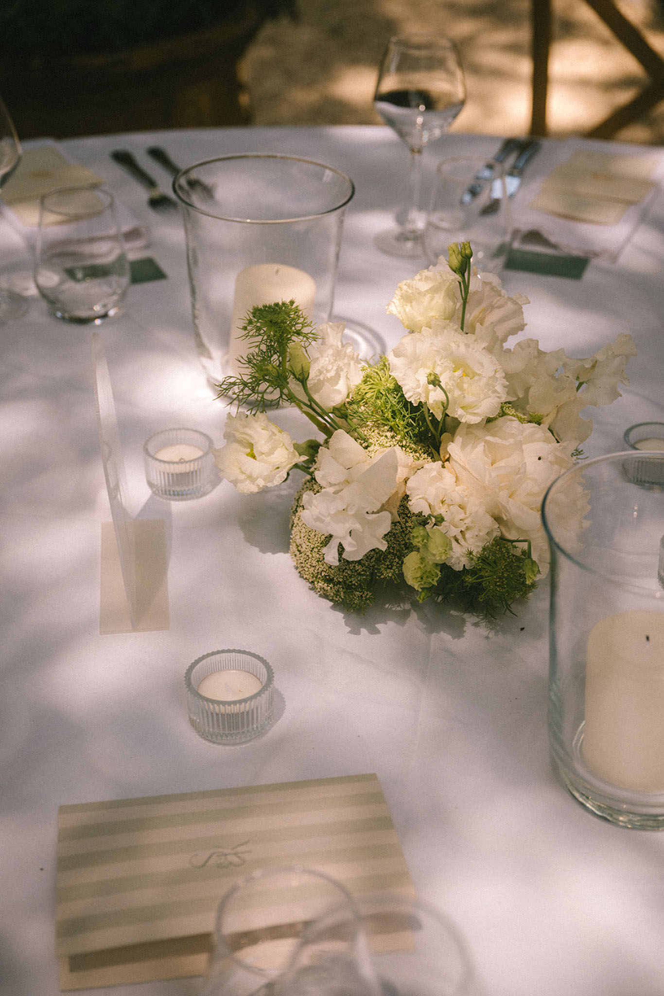 Reception table centerpiece with ivory lisianthus white sweet peas hurricane candles and striped menu cards