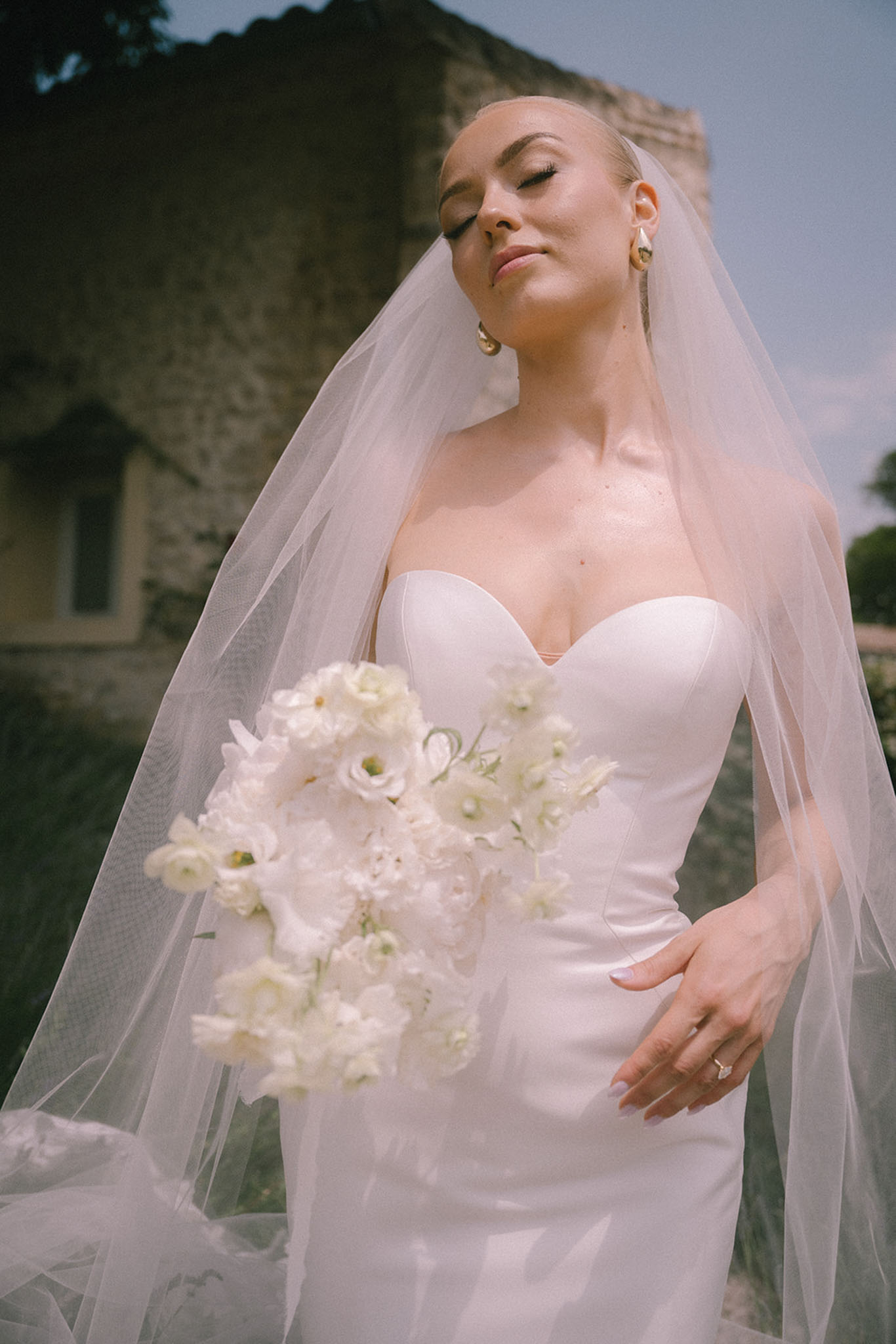 Bride with eyes closed holding white lisianthus and sweet pea bouquet in ivory satin gown