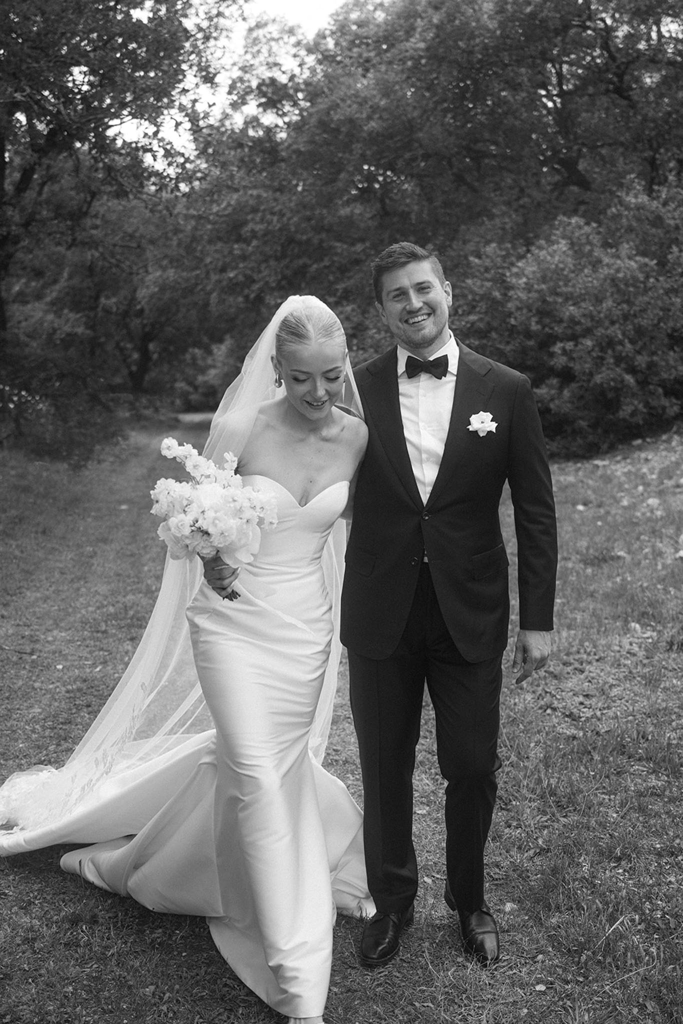 Black and white couple walking tree-lined path bride in strapless satin gown with cathedral veil and bouquet