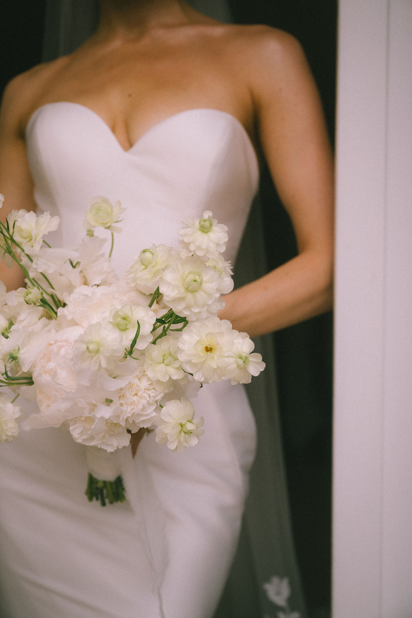 Close-up of bride holding white peony and scabiosa bouquet against strapless sweetheart gown