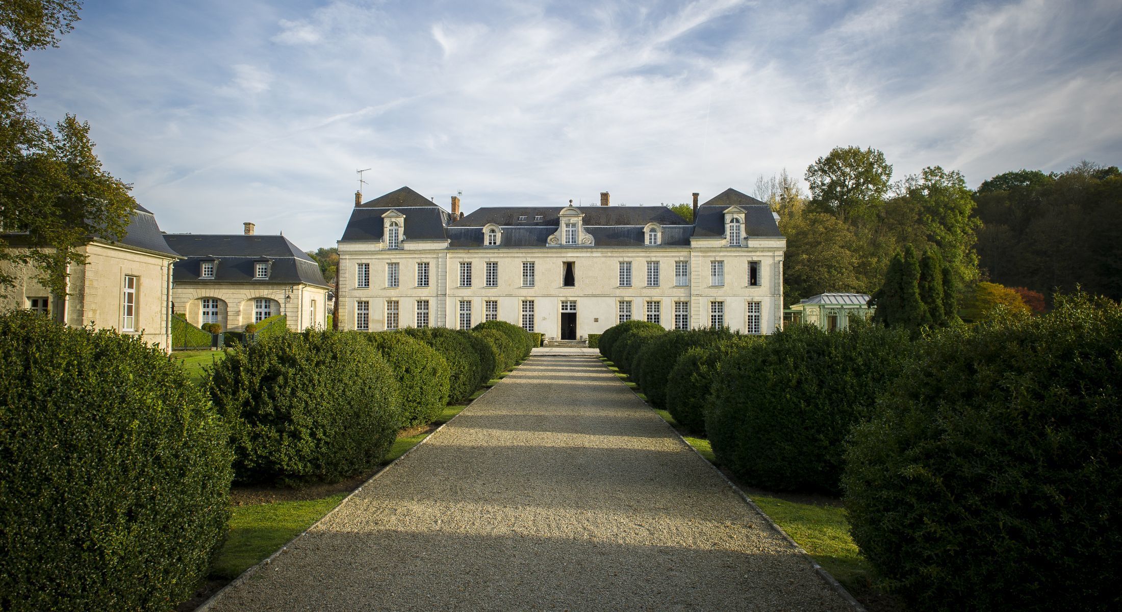 French chateau with limestone facades and slate mansard roof, gravel driveway lined with clipped box hedges