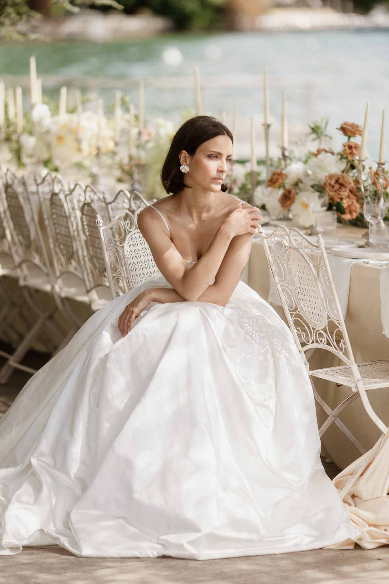 Bride seated at waterside tablescape with ivory and terracotta rose centrepieces and wrought-iron chairs