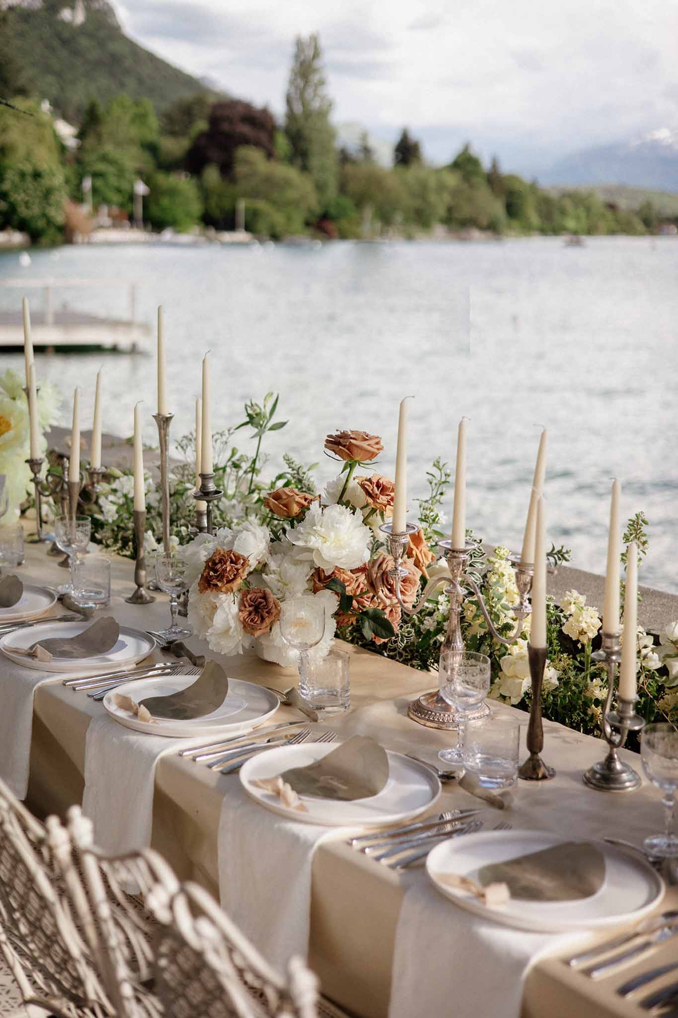Lakeside reception table with terracotta roses, white peonies, silver candlesticks, and mountain backdrop