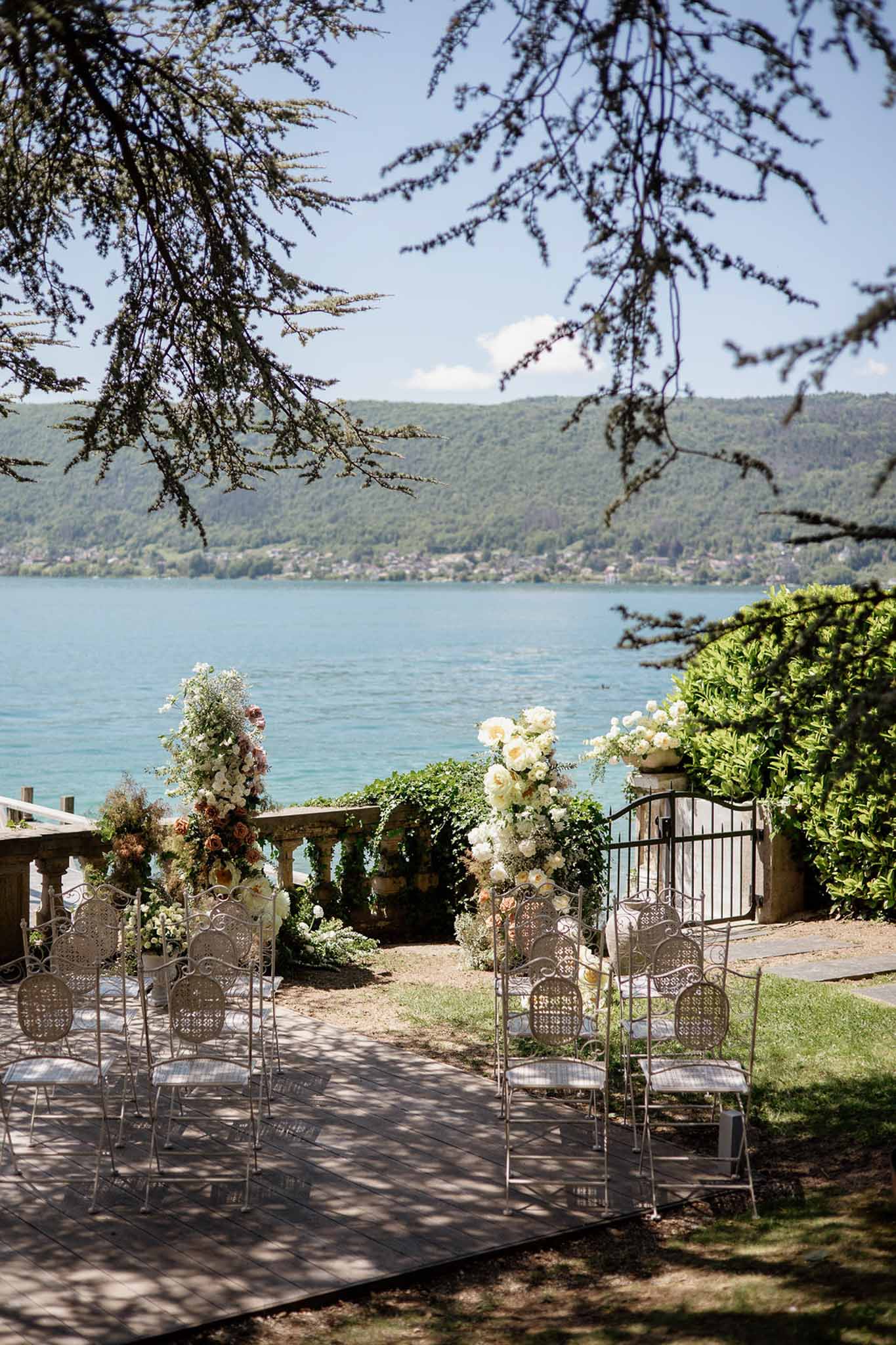 Lakeside ceremony setup with wrought-iron chairs and cream and peach rose arrangements overlooking turquoise lake