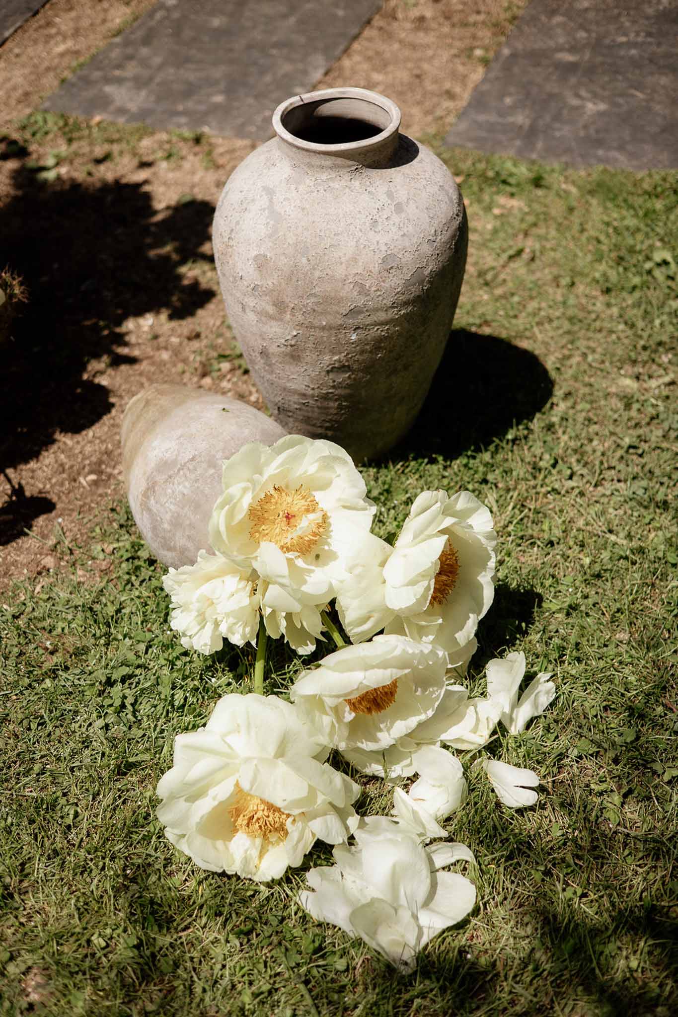 White peonies with golden centers placed beside weathered stone urns on garden paving