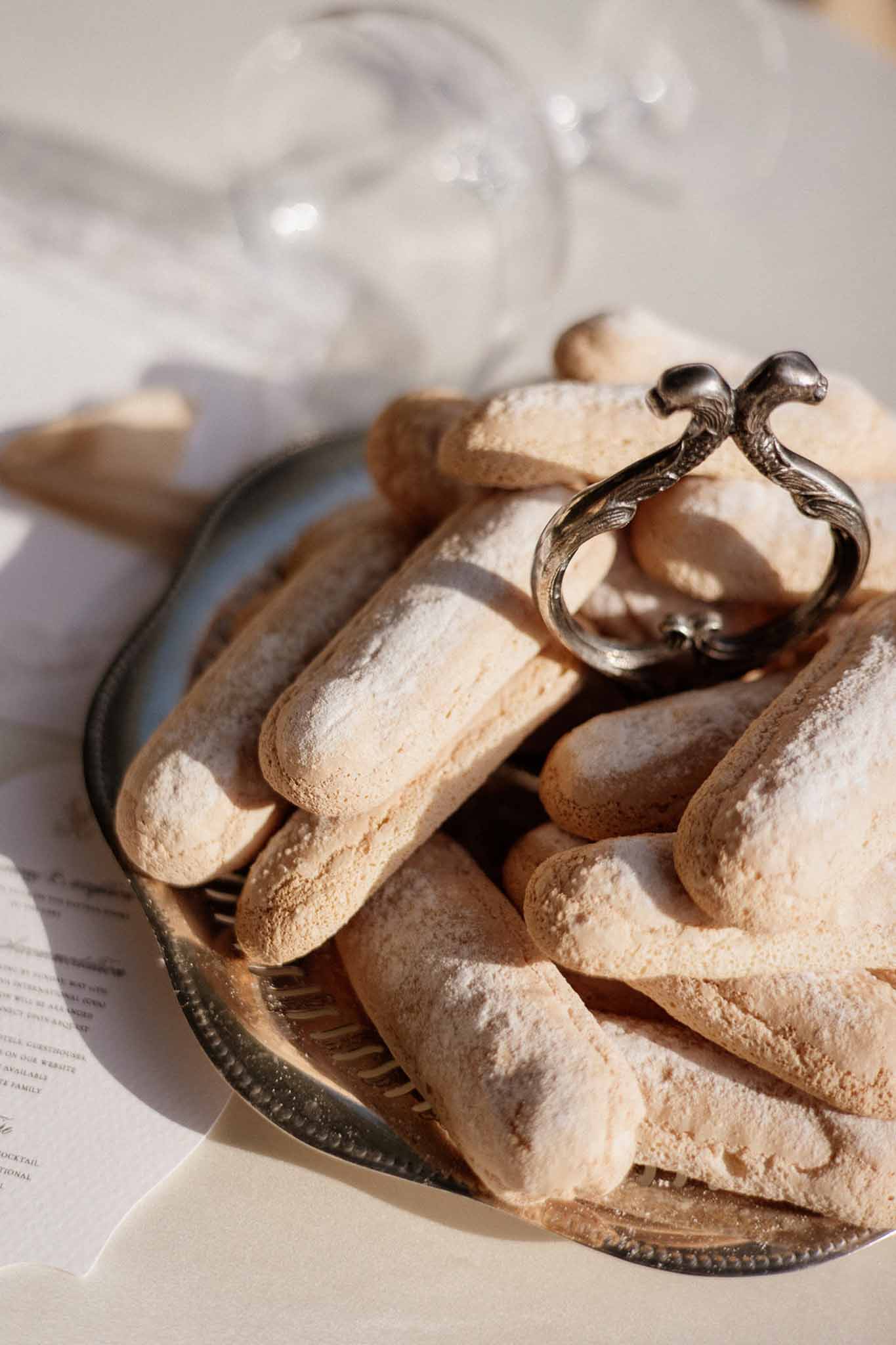 Silver scallop tray of powdered sugar ladyfingers with sculptural napkin ring on white linen table