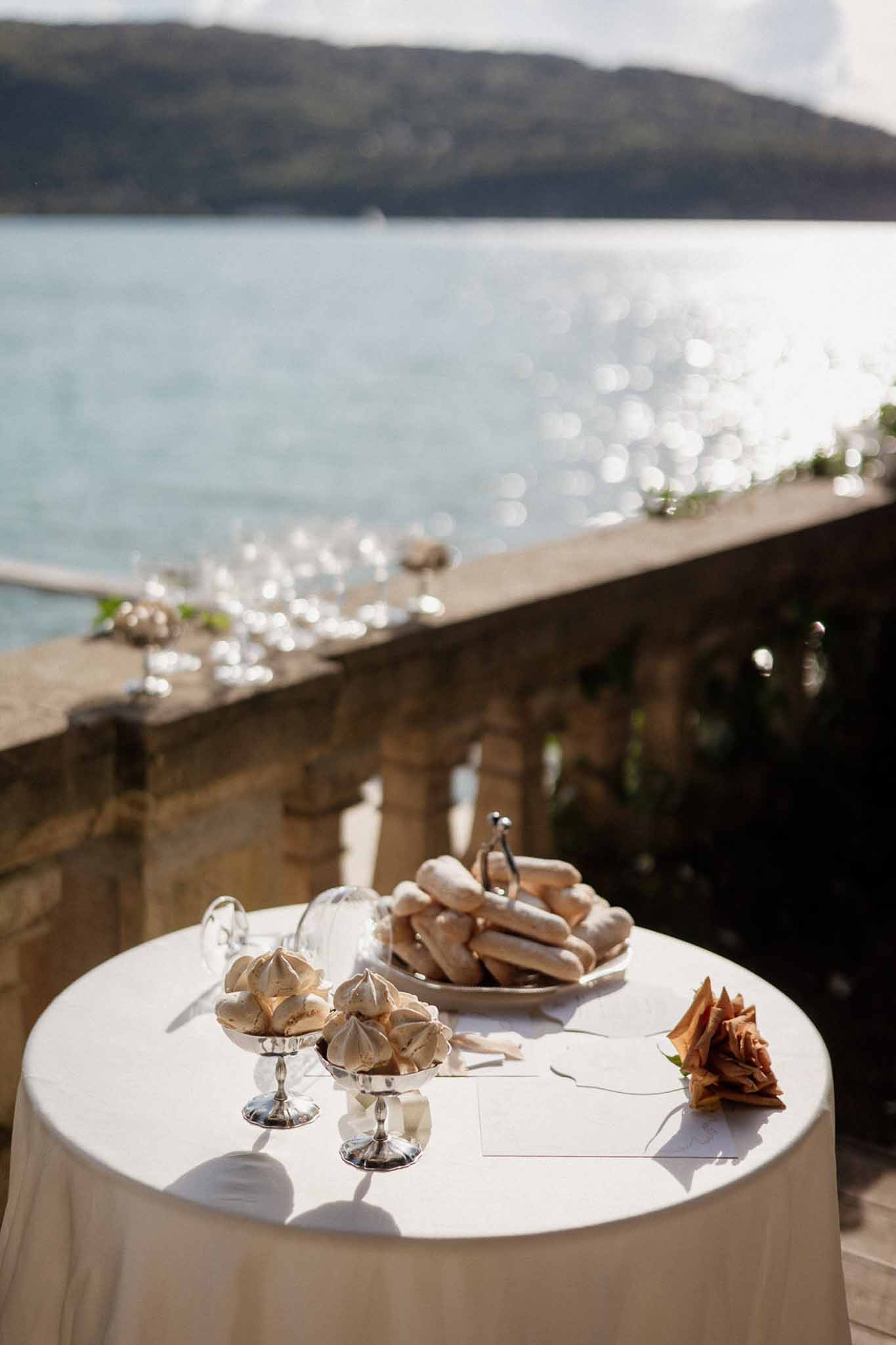 Cocktail table with meringues and ladyfingers on silver stands overlooking lake from stone terrace