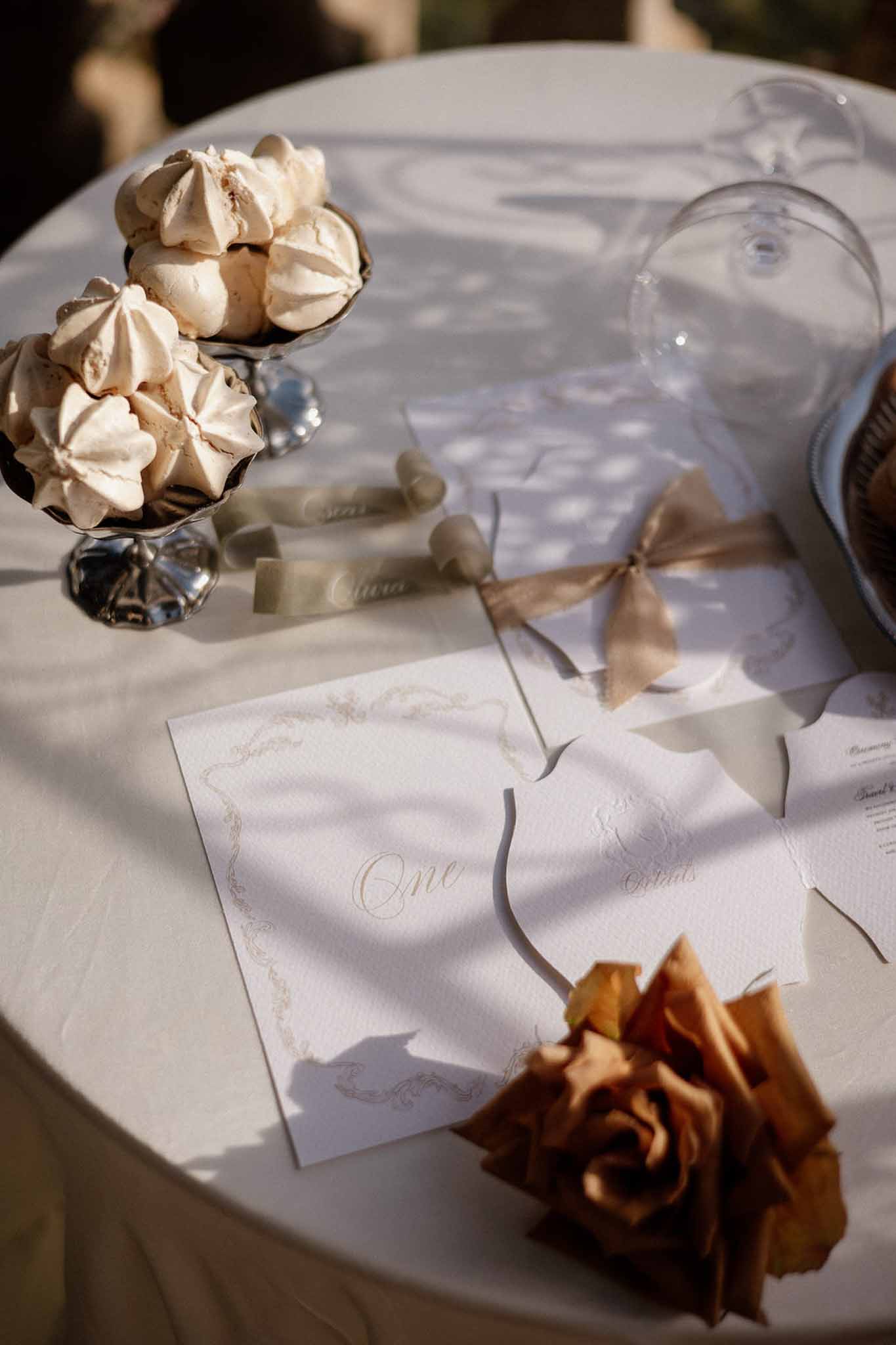 Table number card, menus in gold calligraphy, meringue dish, and amber rose on cream linen