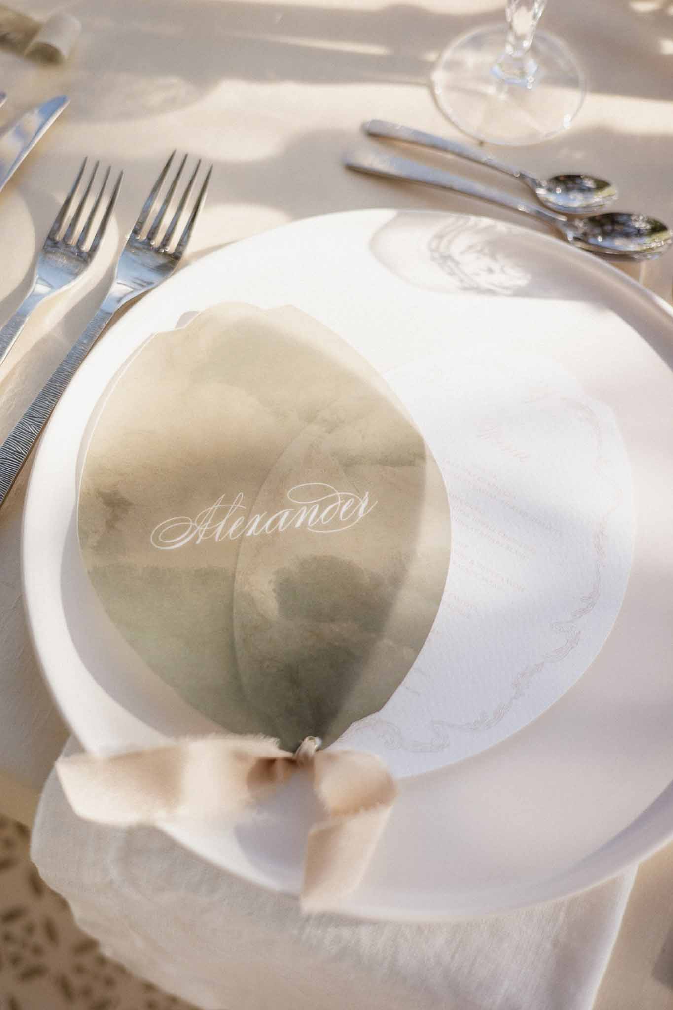 Place setting with pressed leaf name card tied with taupe ribbon on white charger and linen