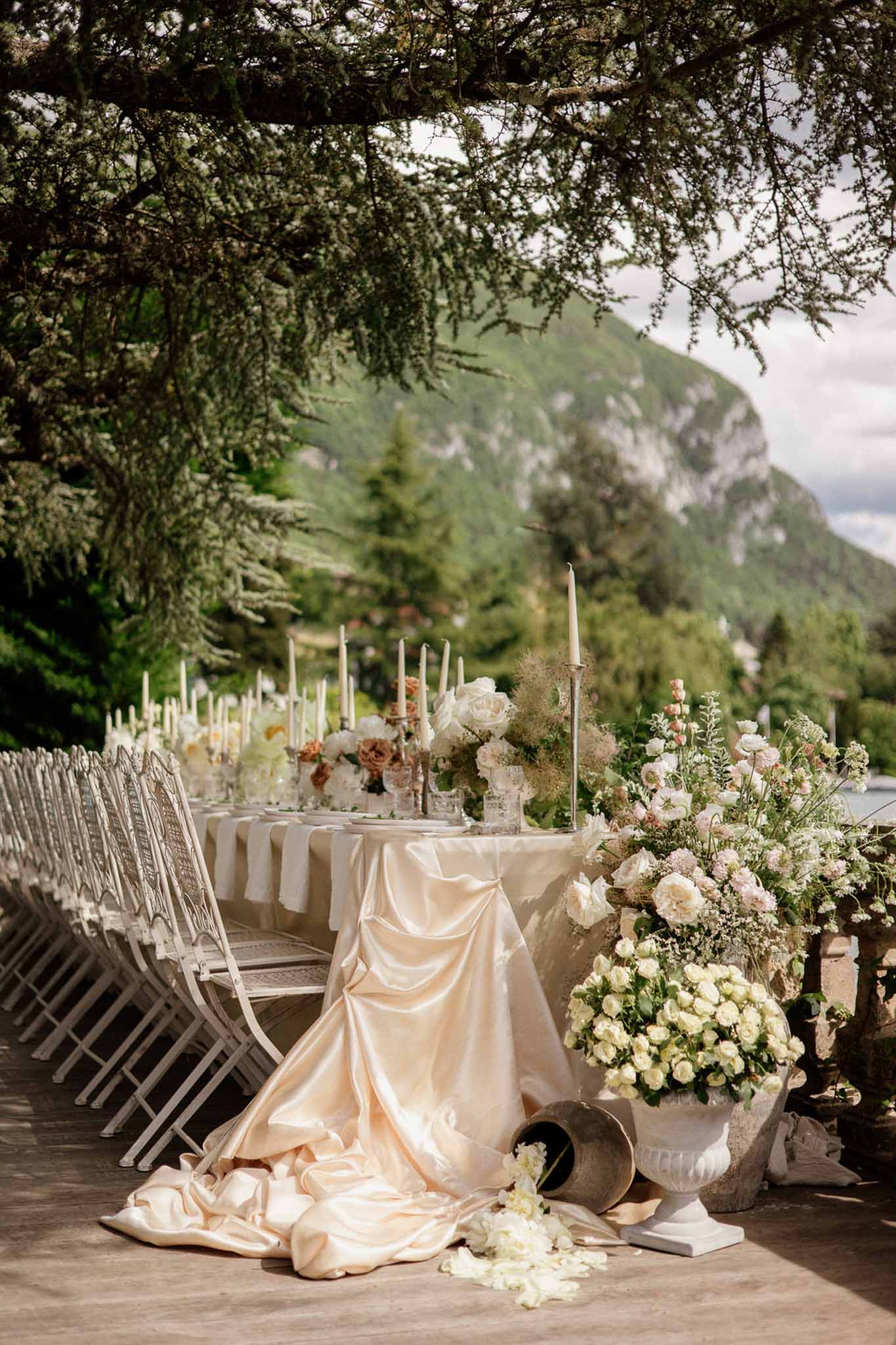 Long reception table on terrace with champagne linen ivory roses taper candles and mountain backdrop