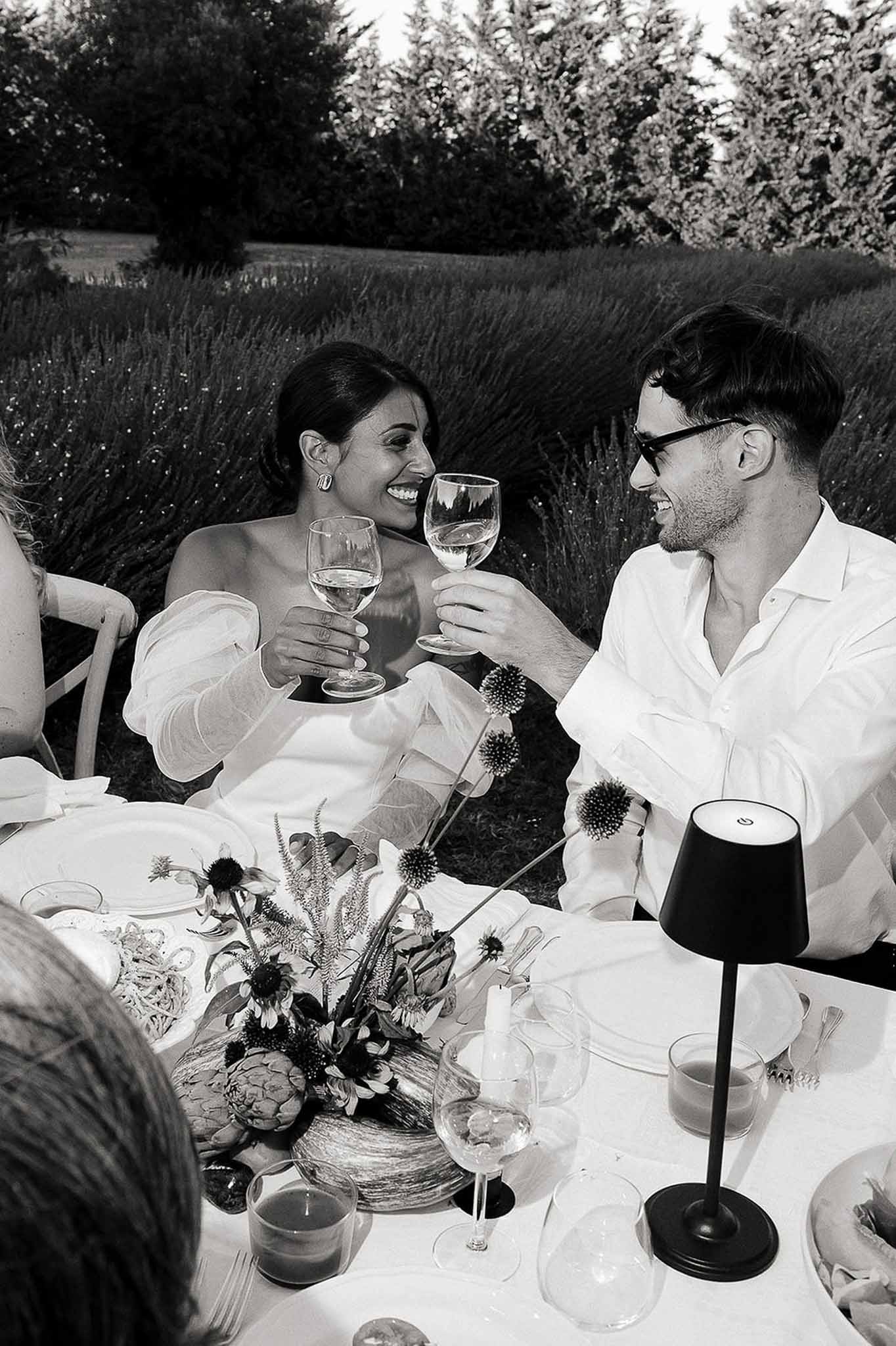 Bride and groom seated at reception table raising champagne glasses for a toast, Bastide des Barattes
