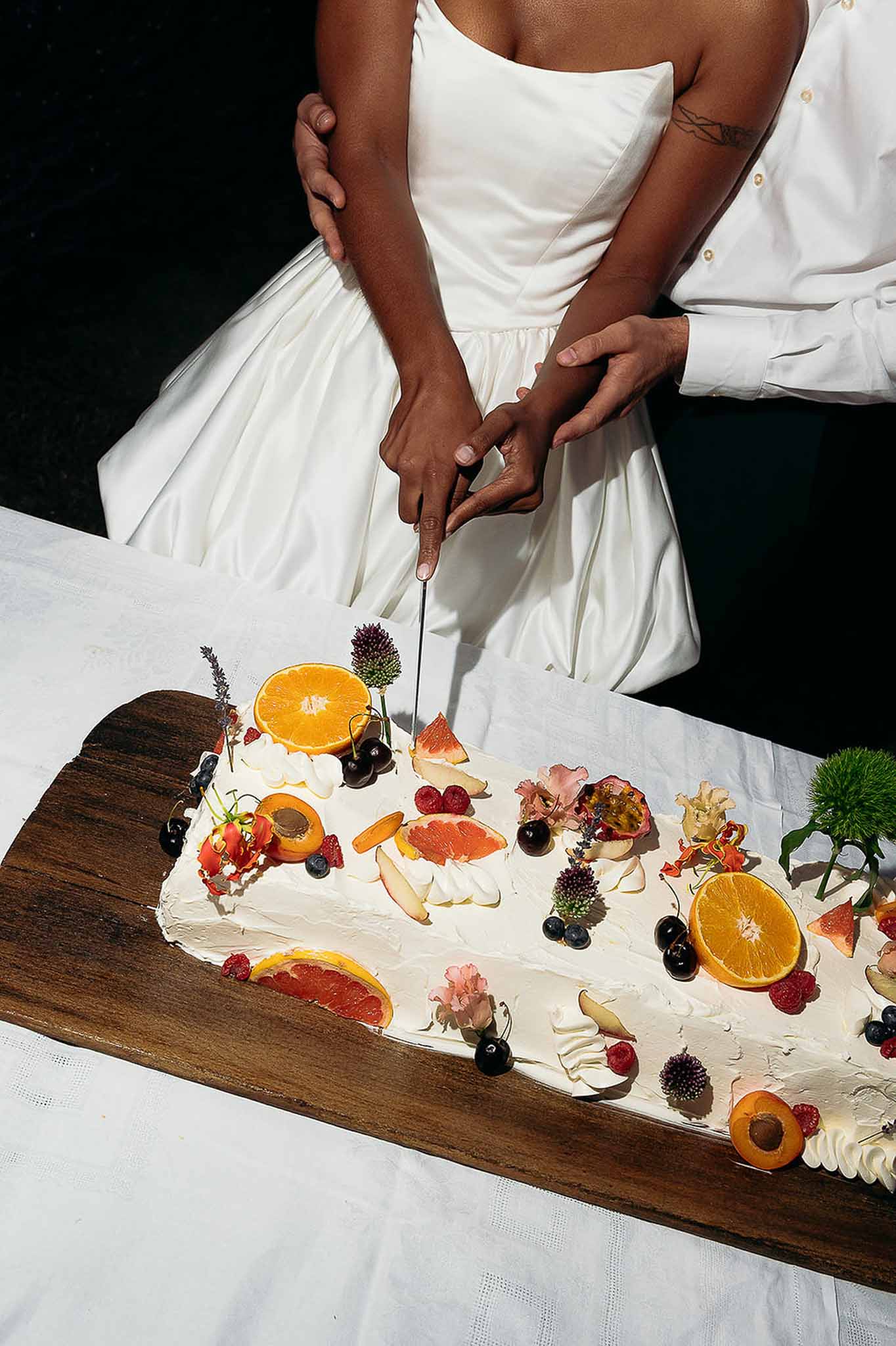 Couple hugging beside fruit-topped wedding cake during the cutting ceremony, Bastide des Barattes