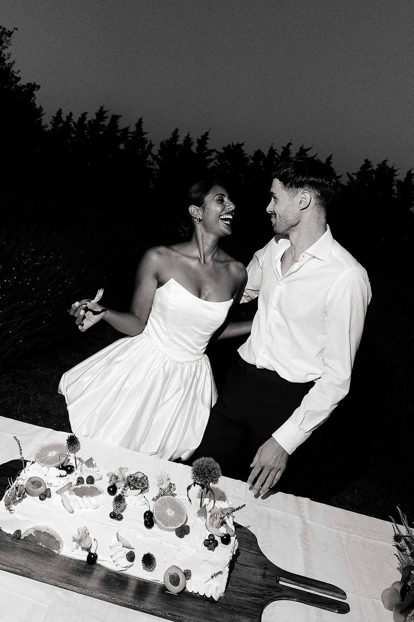 Black and white photo of couple hugging by the fruit wedding cake at Bastide des Barattes reception