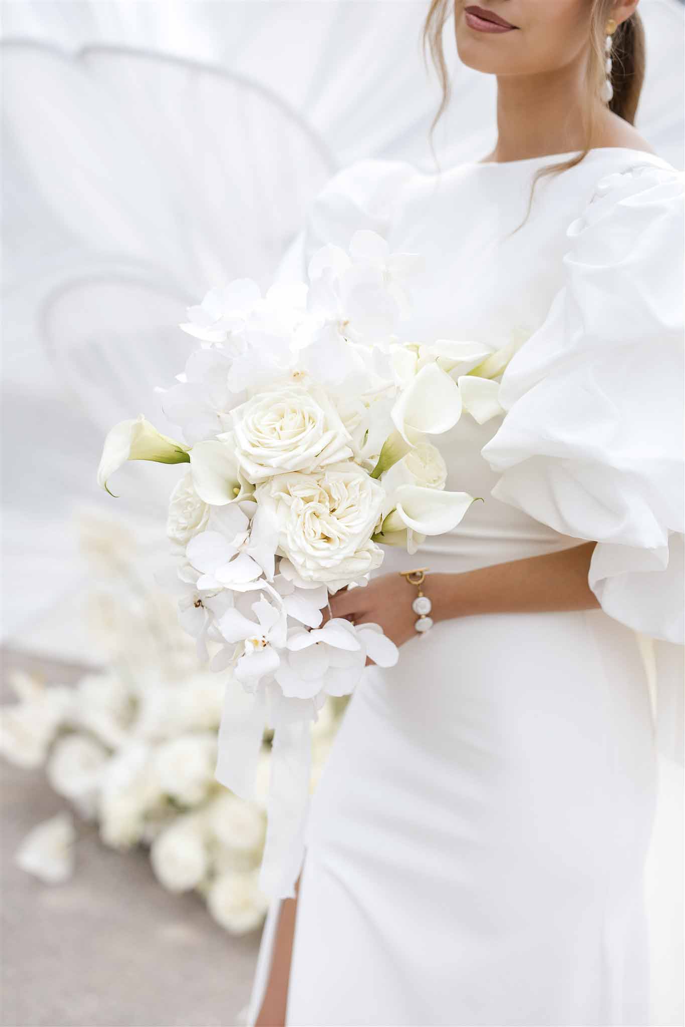 Bride holds cascading white rose, calla lily, and orchid bouquet with ruffled statement sleeves