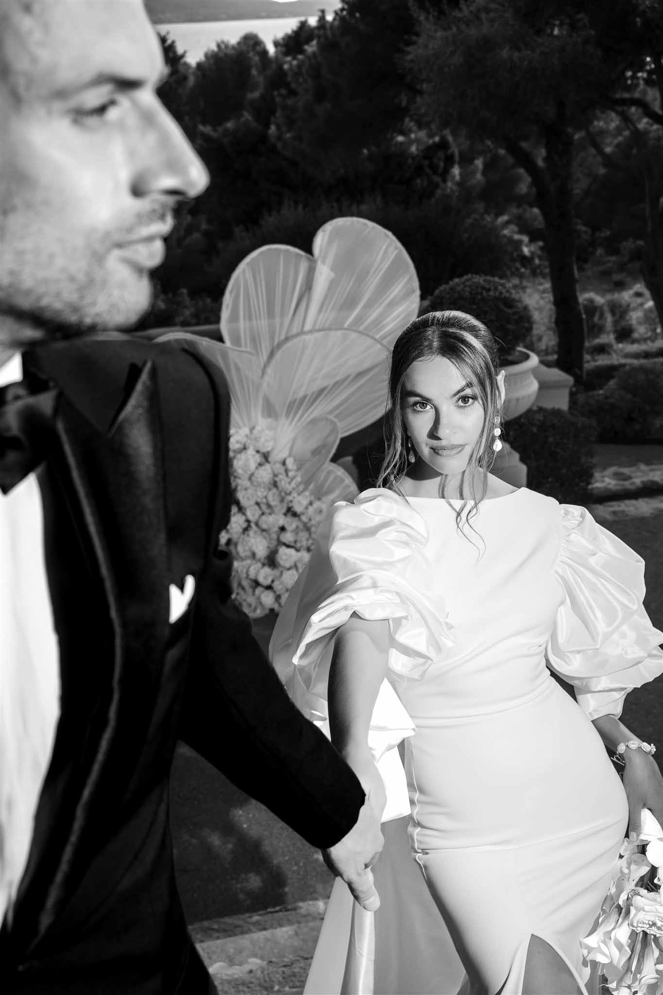 Black and white portrait of bride in puff-sleeve gown with sculptural floral installation behind