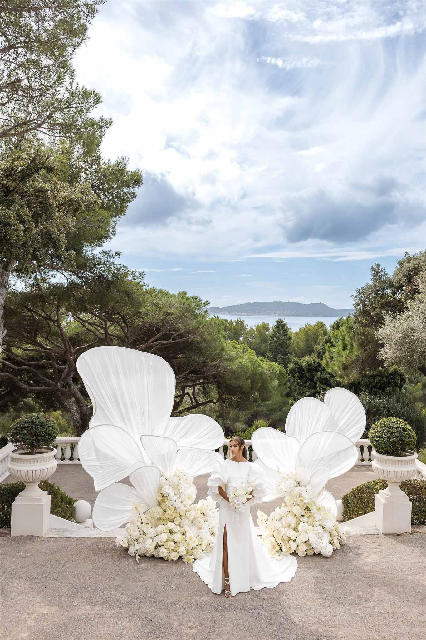 Bride on coastal terrace with oversized white sculptural floral installation and sea view in South of France