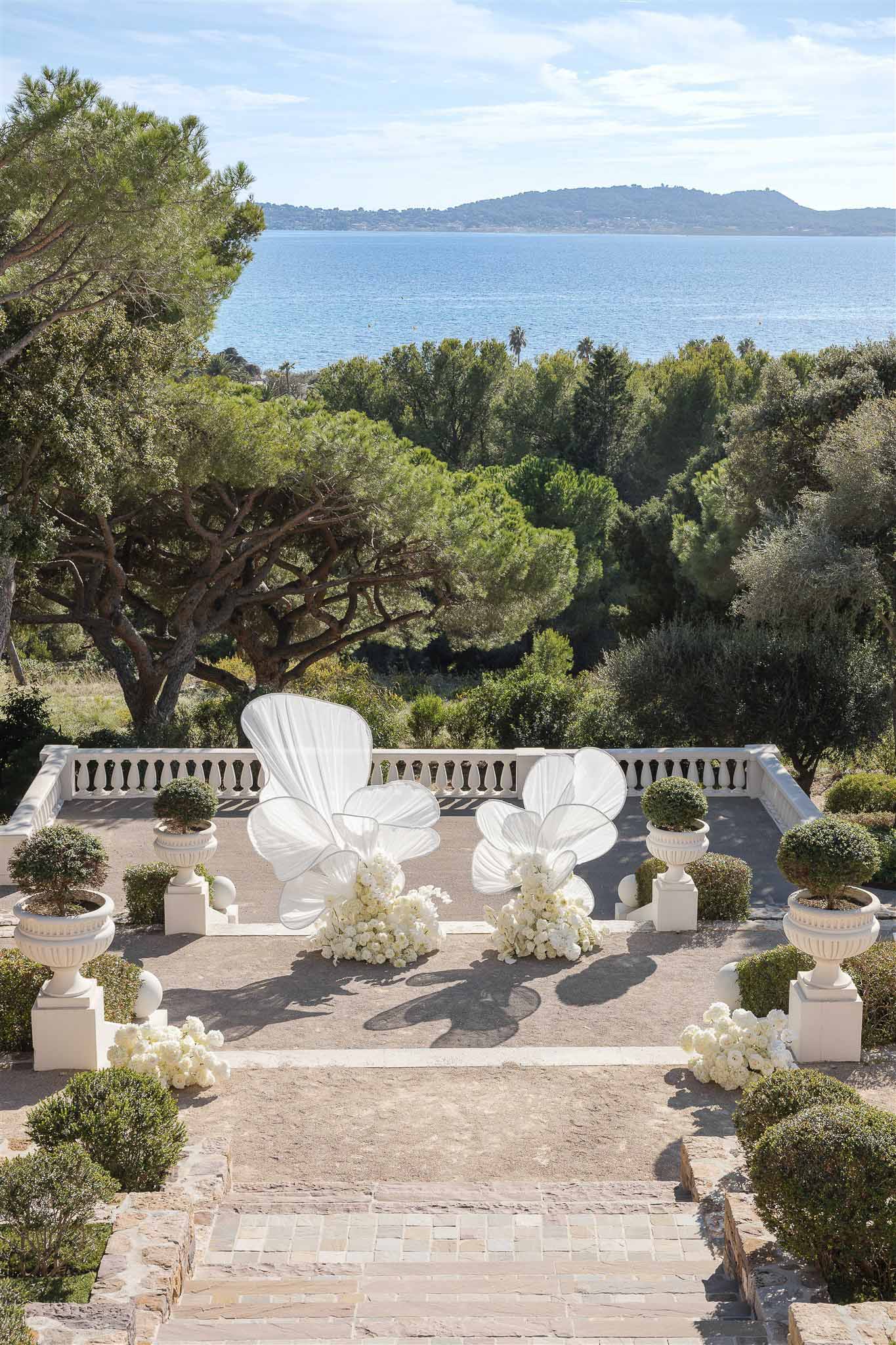 Outdoor ceremony setup on seaside terrace with white fabric sculptures and rose arrangements